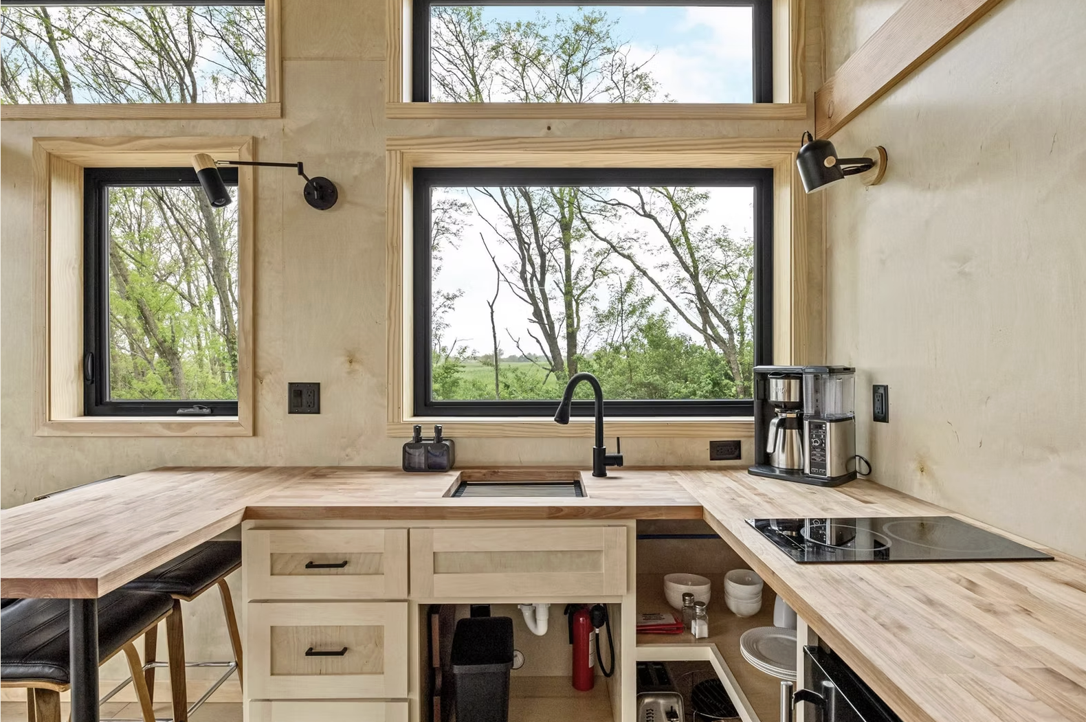 Kitchen with three large windows showing trees outside, wooden countertops, a black faucet, coffee maker, stove, and stools. Iowa City. Stecker Home Services. Home Renovations. Iowa City Contractor. 