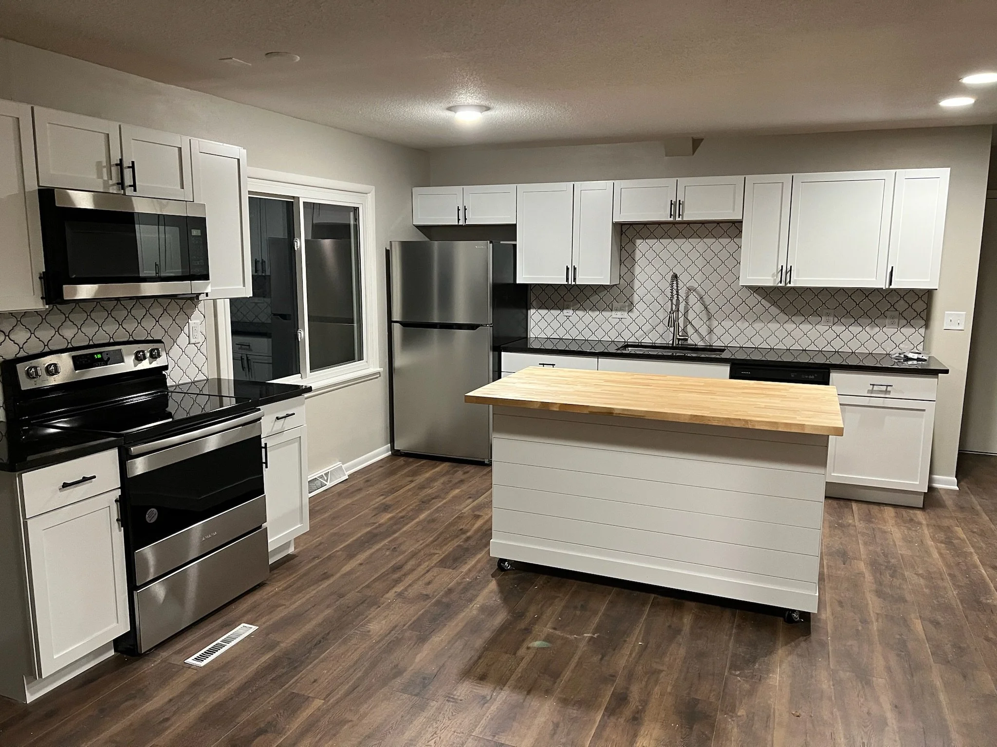 A modern kitchen with white cabinets, stainless steel appliances, a wooden island, and wood flooring. Iowa City. Stecker Home Services. Home Renovations. Iowa City Contractor. 