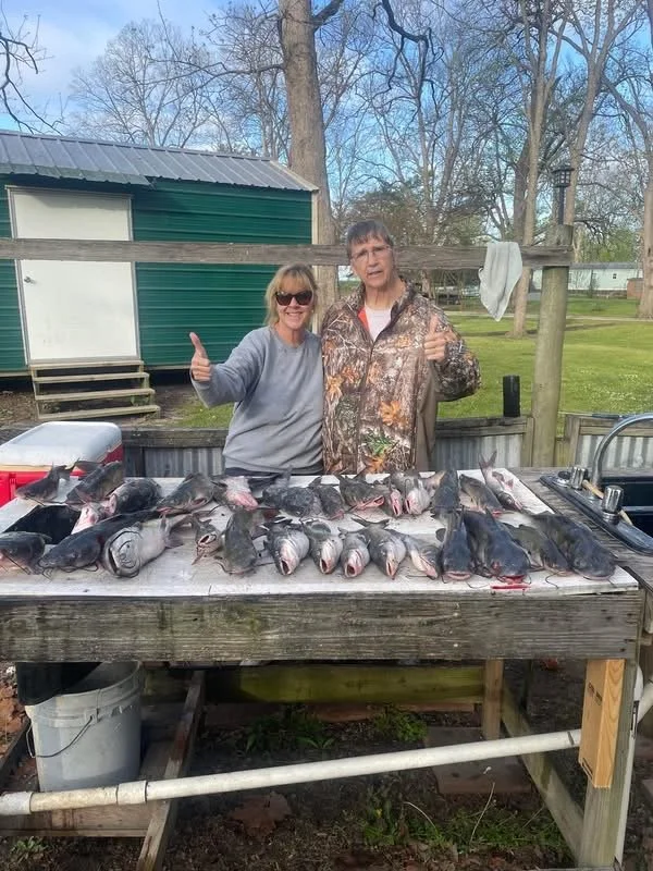 Two happy campers with a table full of freshly caught catfish.