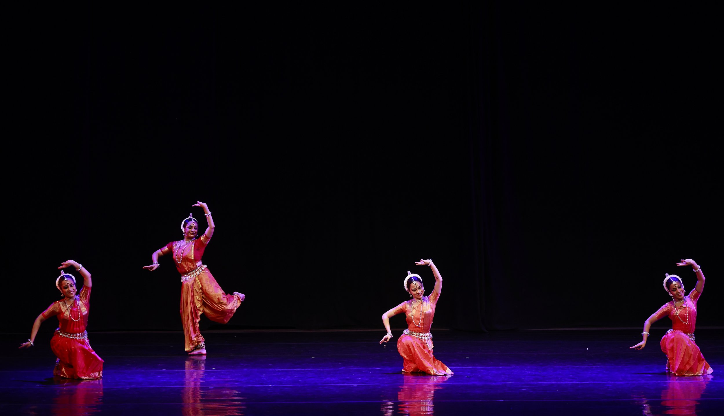 four dancers performing in front of a black backdrop