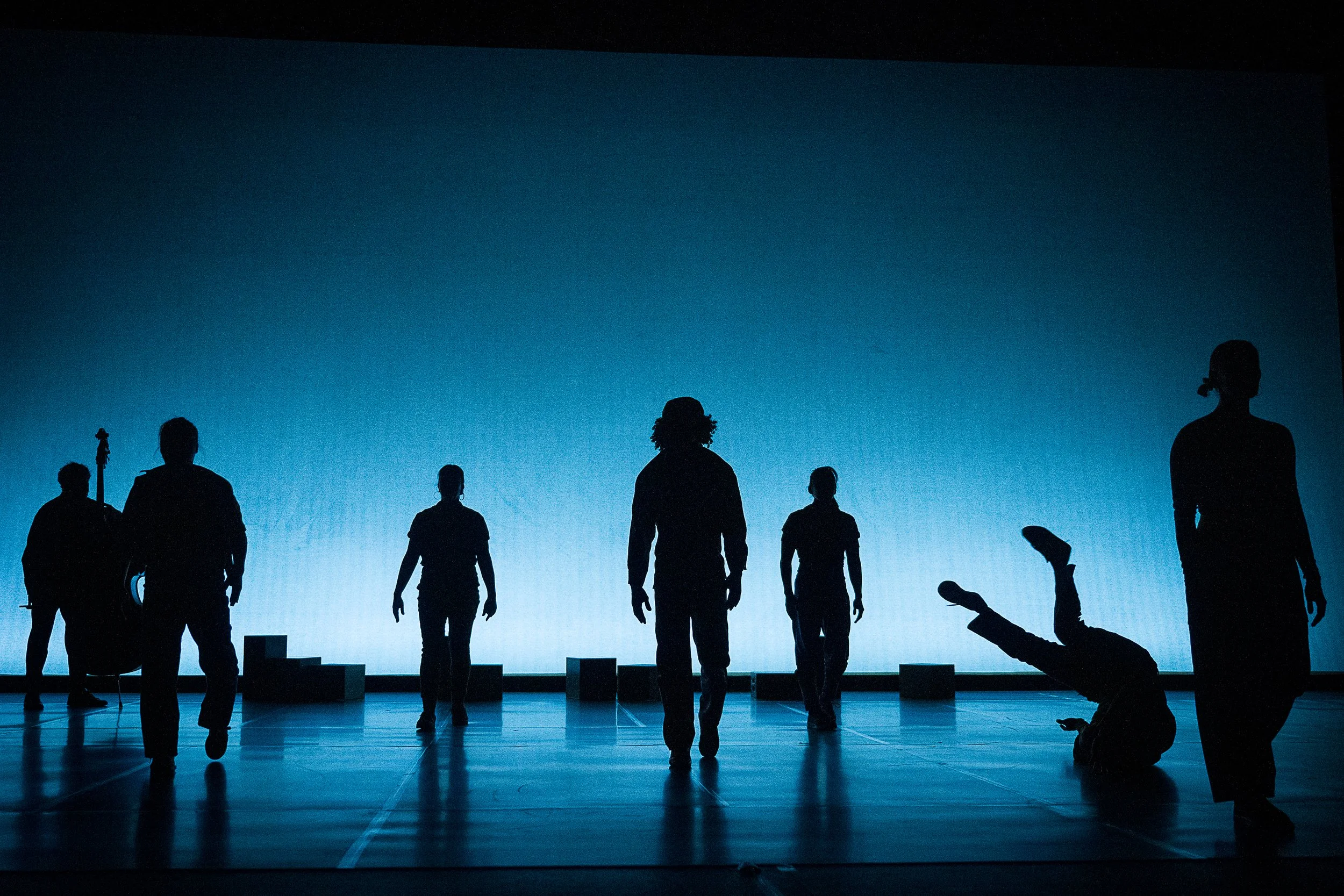 dancers and musicians in silhouette in front of a blue backdrop