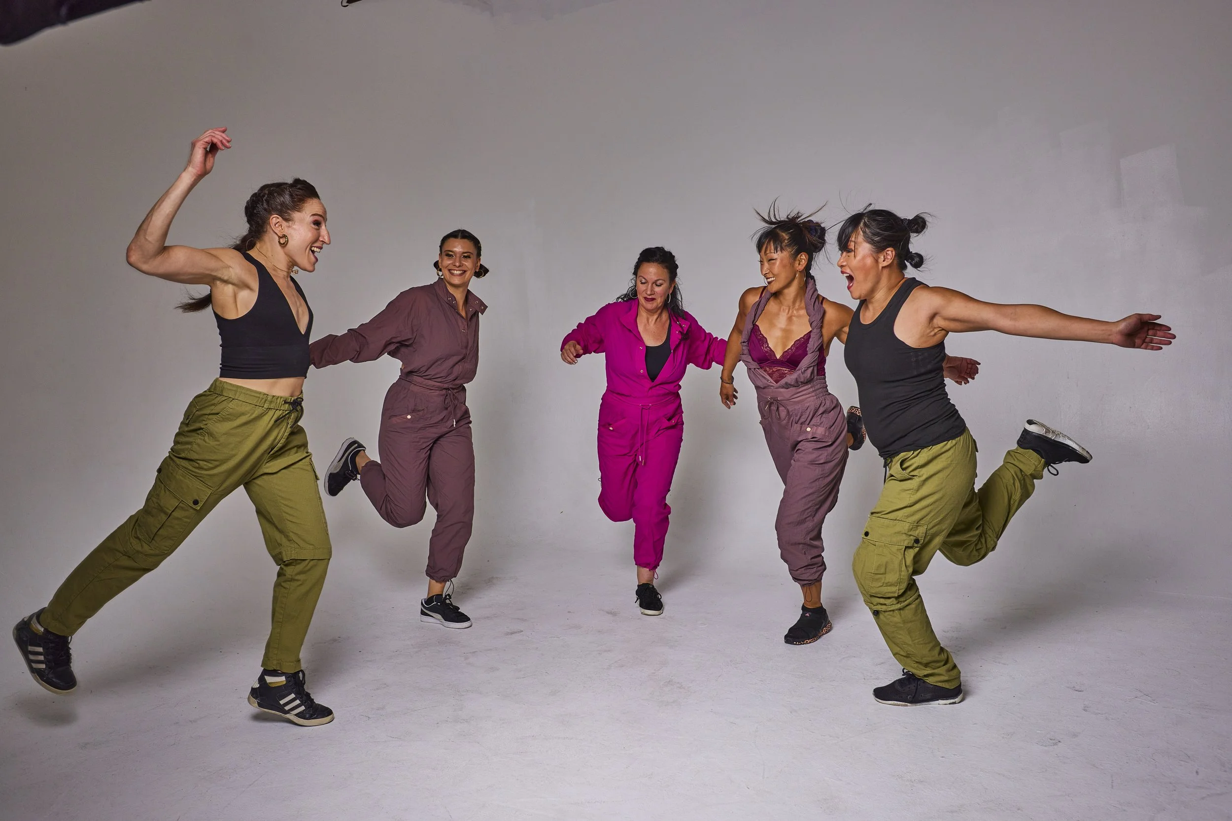 five dancers performing in front of a gray backdrop