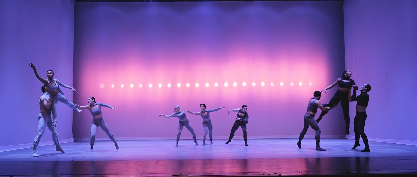 nine dancers in front of a bright, purple backdrop