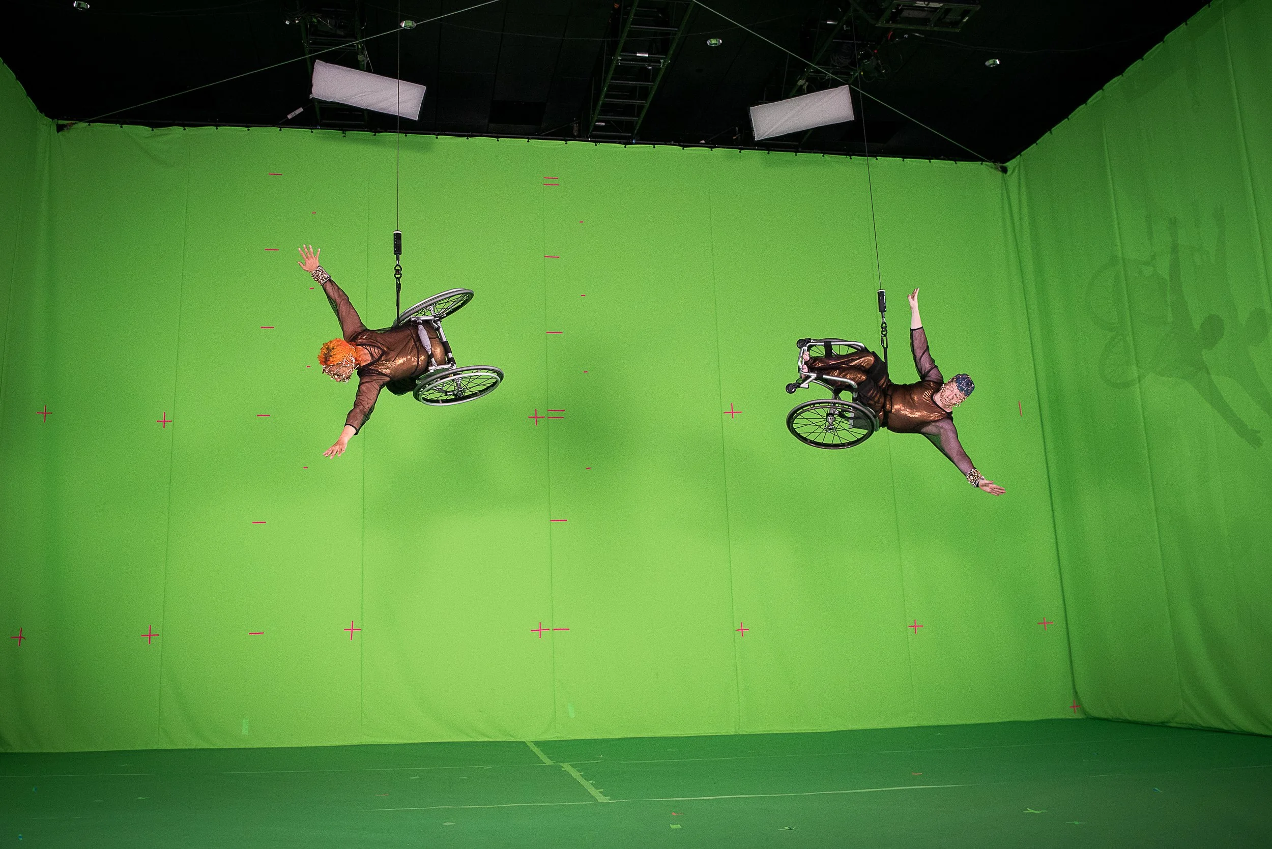 two performers in wheelchairs attached to cords propelling them down toward the floor of the stage