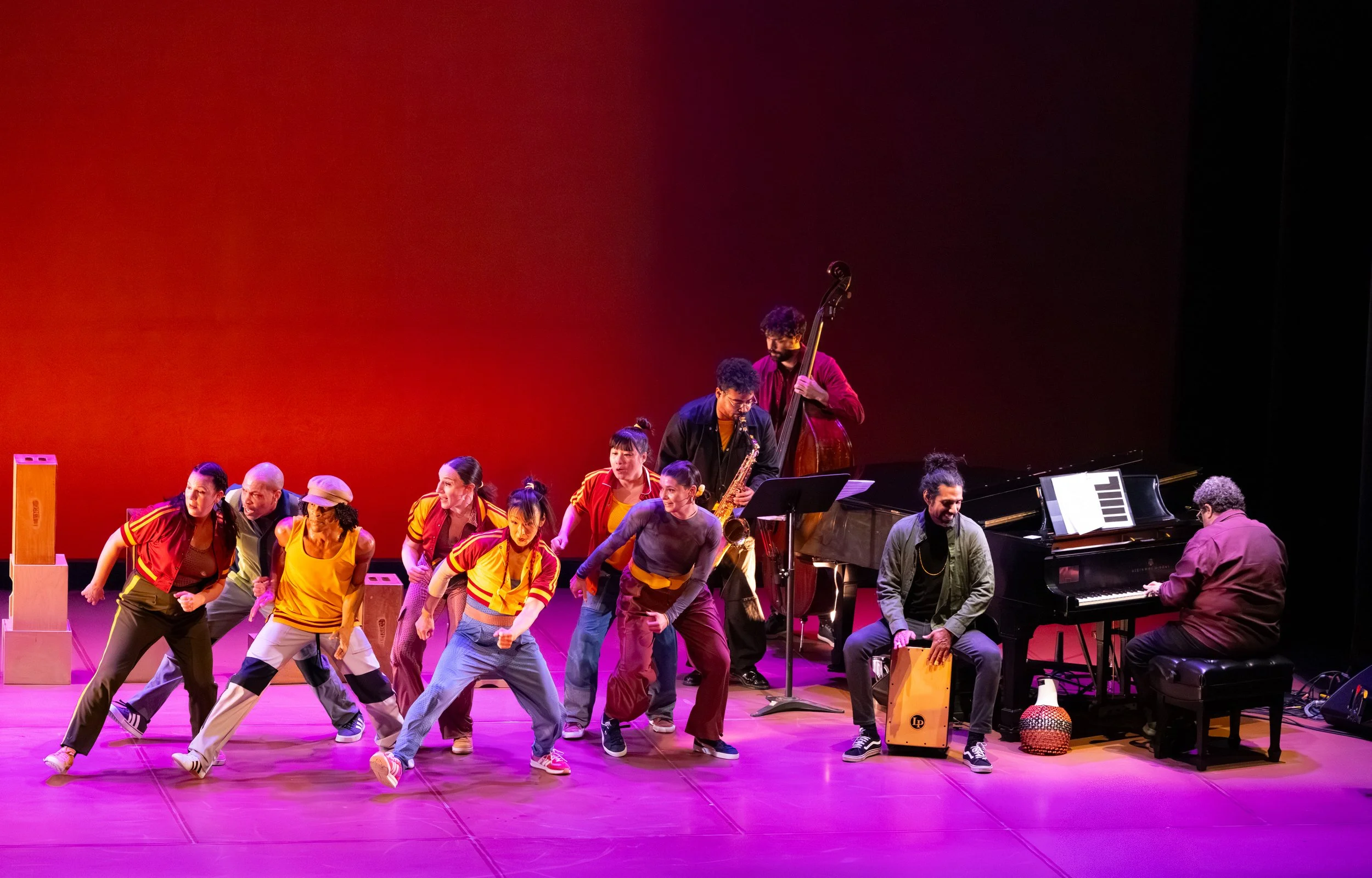 dancers and musicians performing on stage with a red backdrop