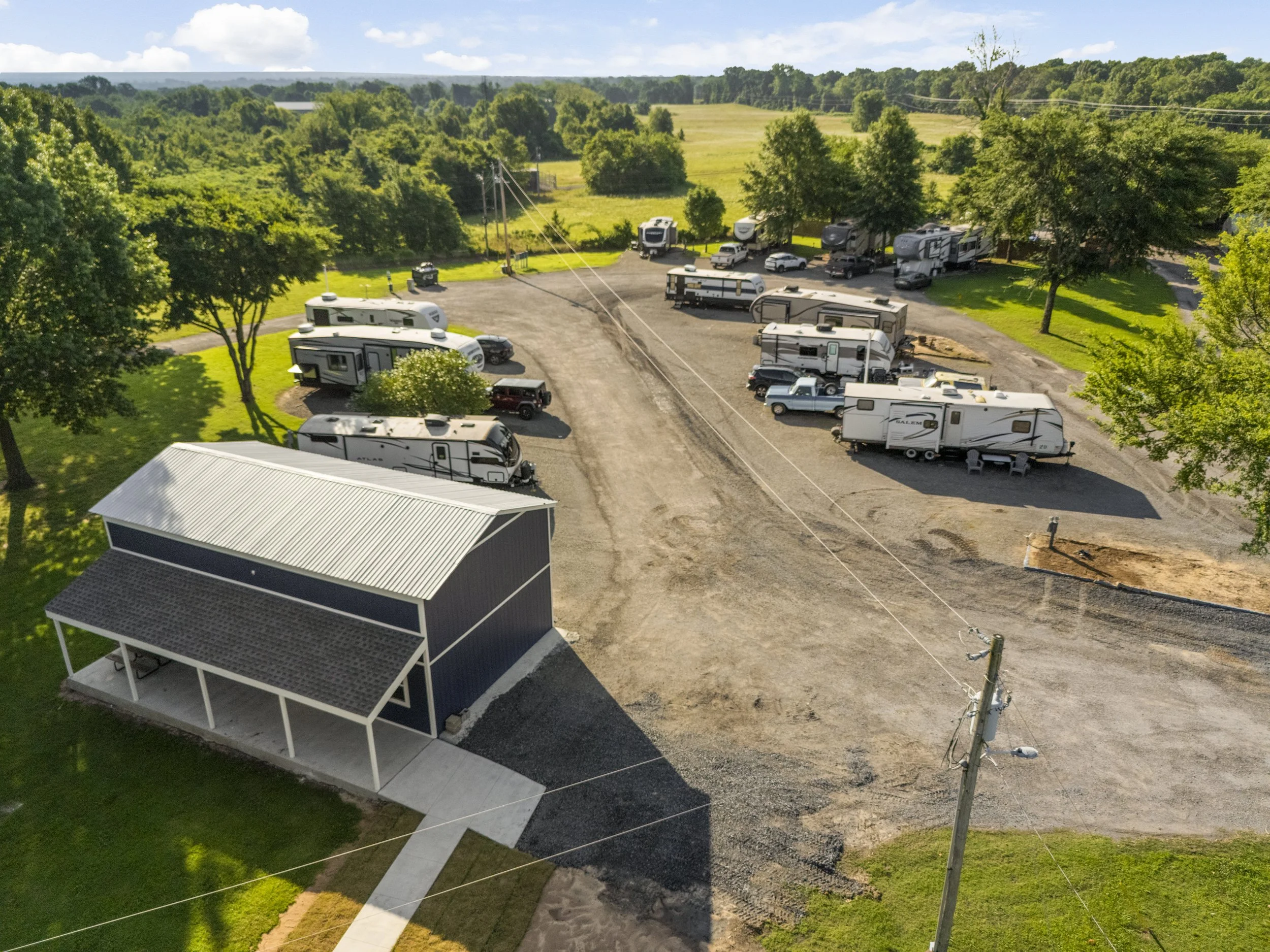 Aerial view of a parking lot filled with RVs, trucks, and cars, surrounded by trees and green landscape.
