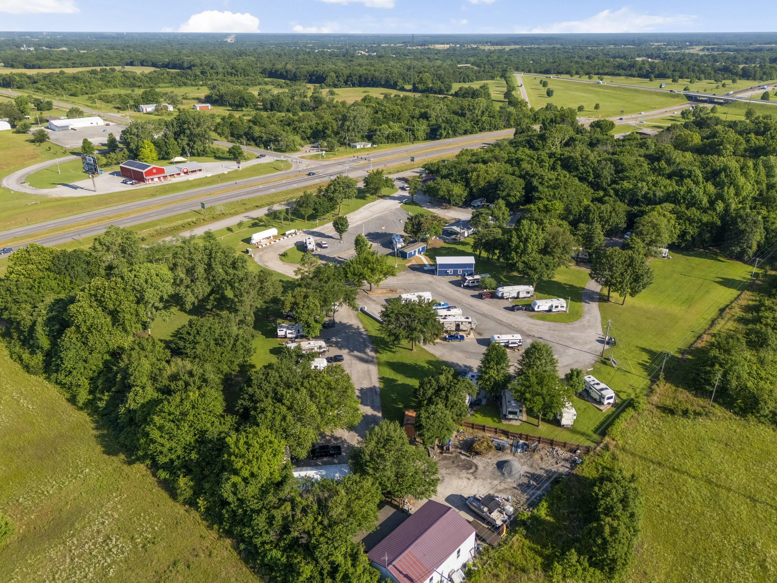 Aerial view of a rural area with trees, roads, a red barn, and several houses and parked RVs.