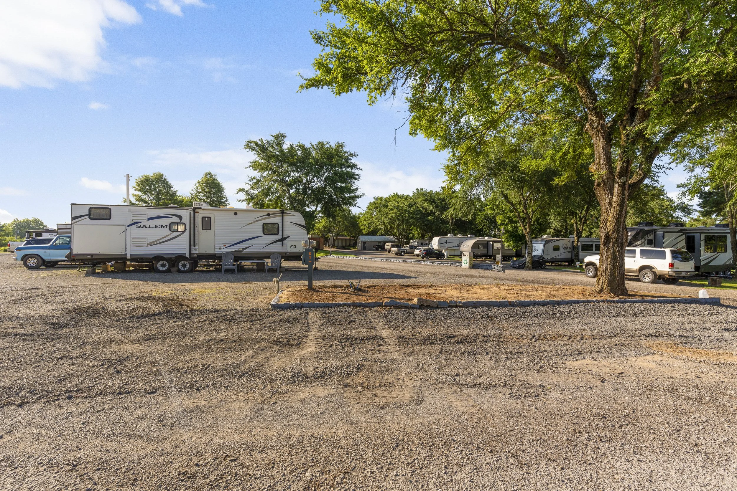 A campground with multiple RVs and vehicles parked under trees on a clear, sunny day.