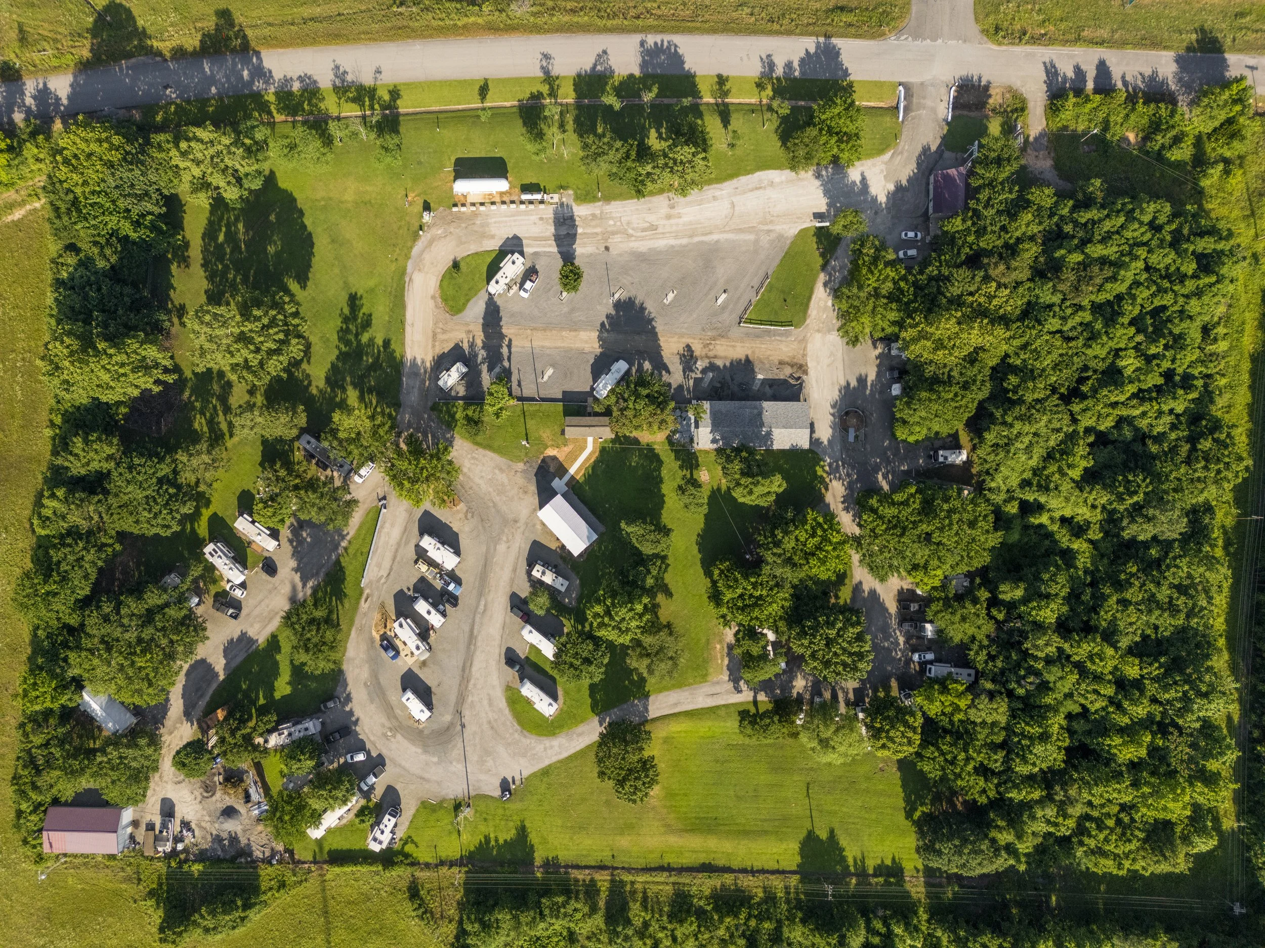 Aerial view of a park with green trees, a gravel parking lot, and residential houses.