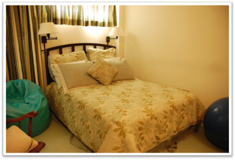 Bedroom with a bed, multiple pillows, nightstands with lamps, a bean bag chair, and a blue exercise ball.