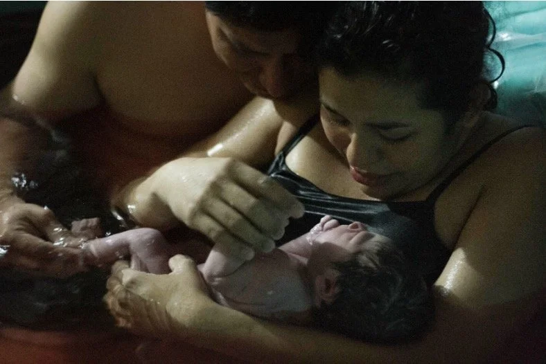 Two women giving birth in water with a newborn baby.