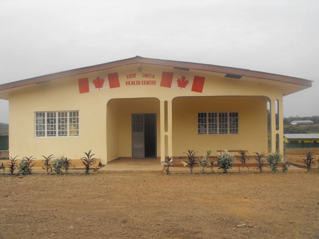 A small yellow health centre building with a sign that reads 'Judy Smith Health Centre' and red maple leaf decorations on the front.