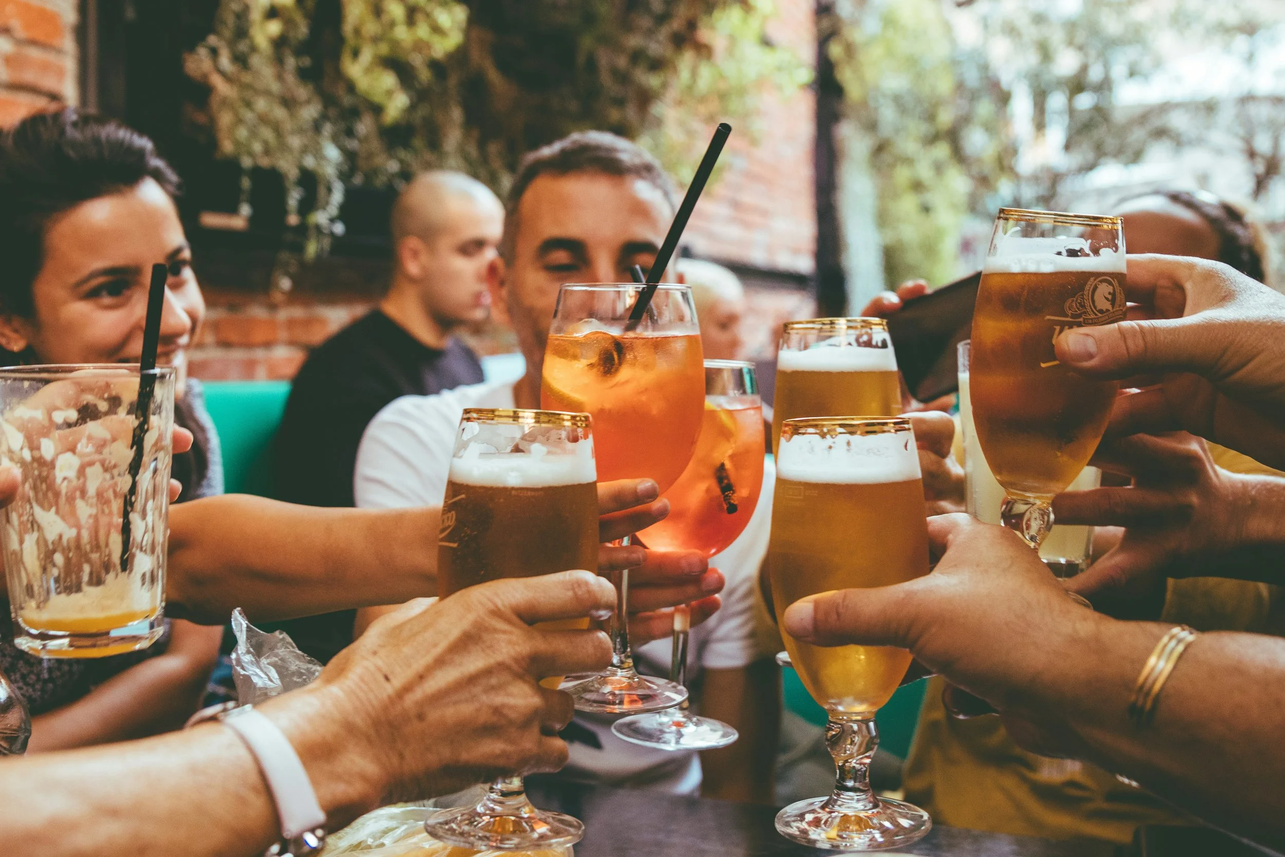 People raising glasses with various drinks in a social gathering at an outdoor or indoor venue.