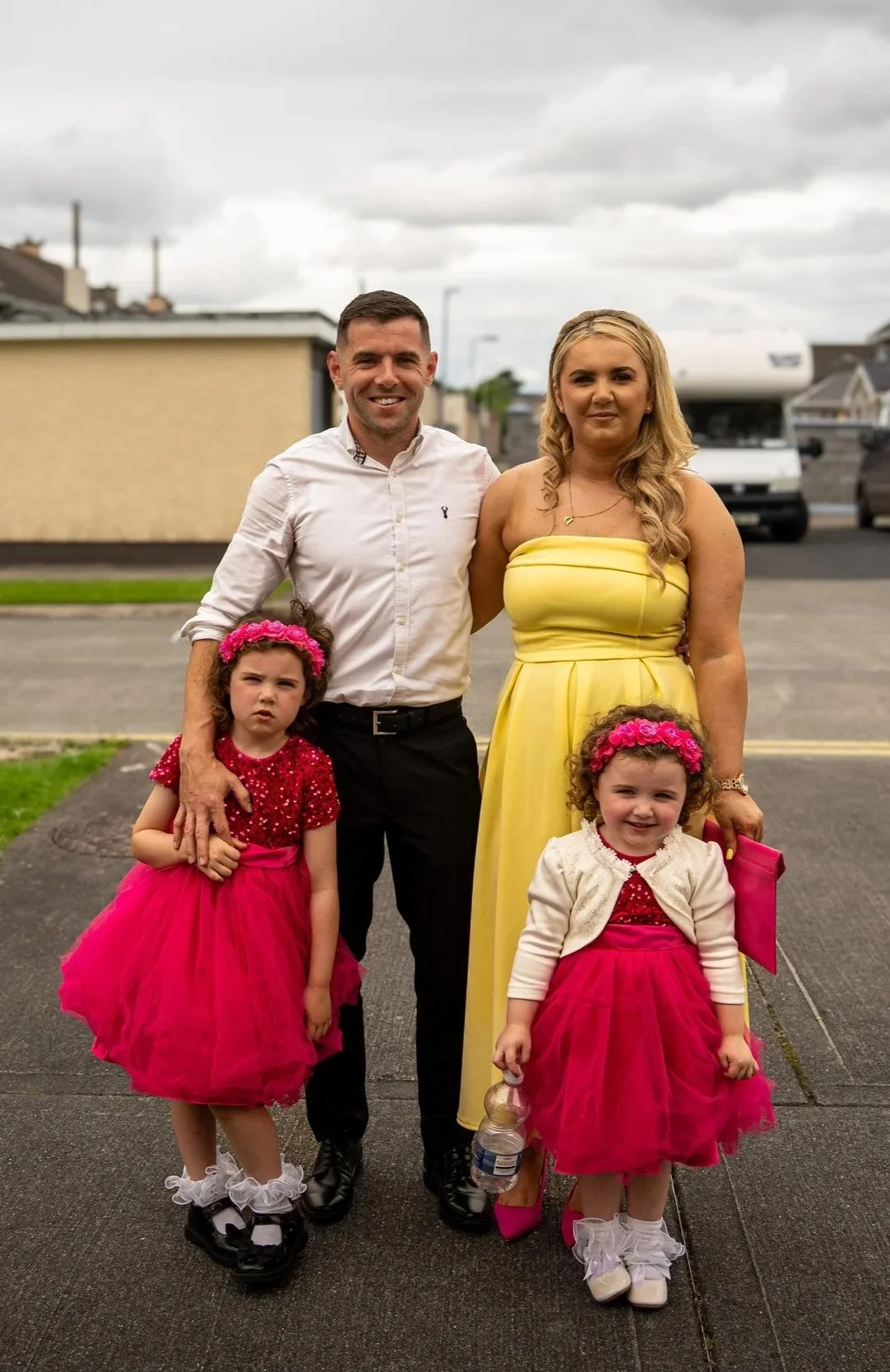 Family photo of two adults and two young girls standing outdoors on a cloudy day.