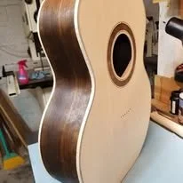 An unfinished acoustic guitar body on a workbench in a workshop.