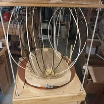 A large circular object with several metal wires or probes sticking out, placed on a wooden base, in a workshop or industrial setting.