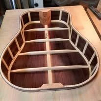The inside of an unfinished guitar body on a workbench, showing wooden frame and hollow sections.