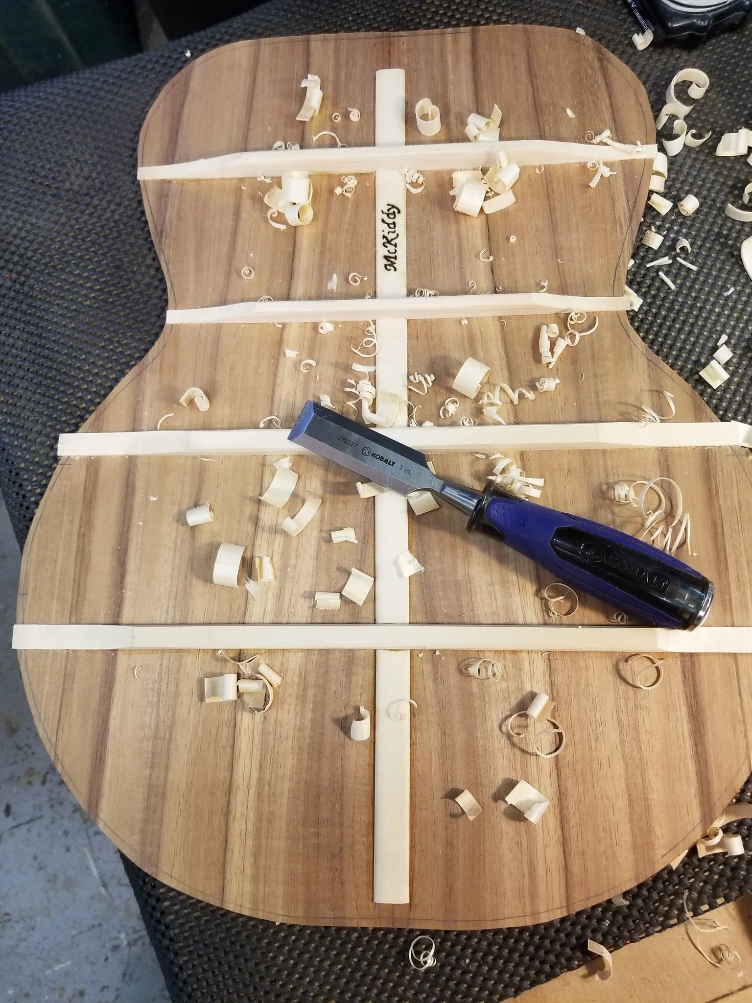 A wooden table with wood shavings, a chisel, and white woodworking strips, labeled with