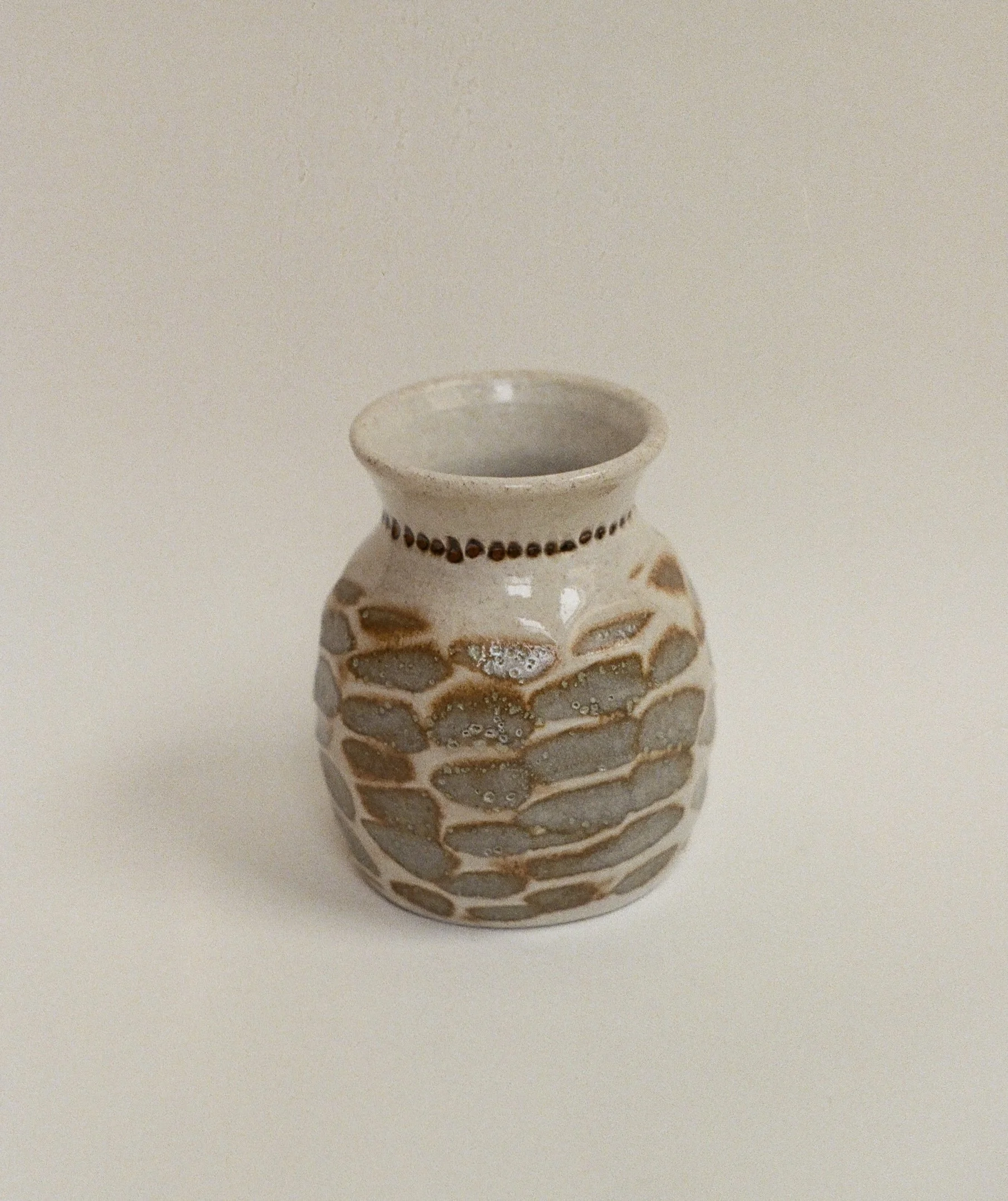 A ceramic vase with a honeycomb pattern in light brown and gray, placed on a plain white surface.