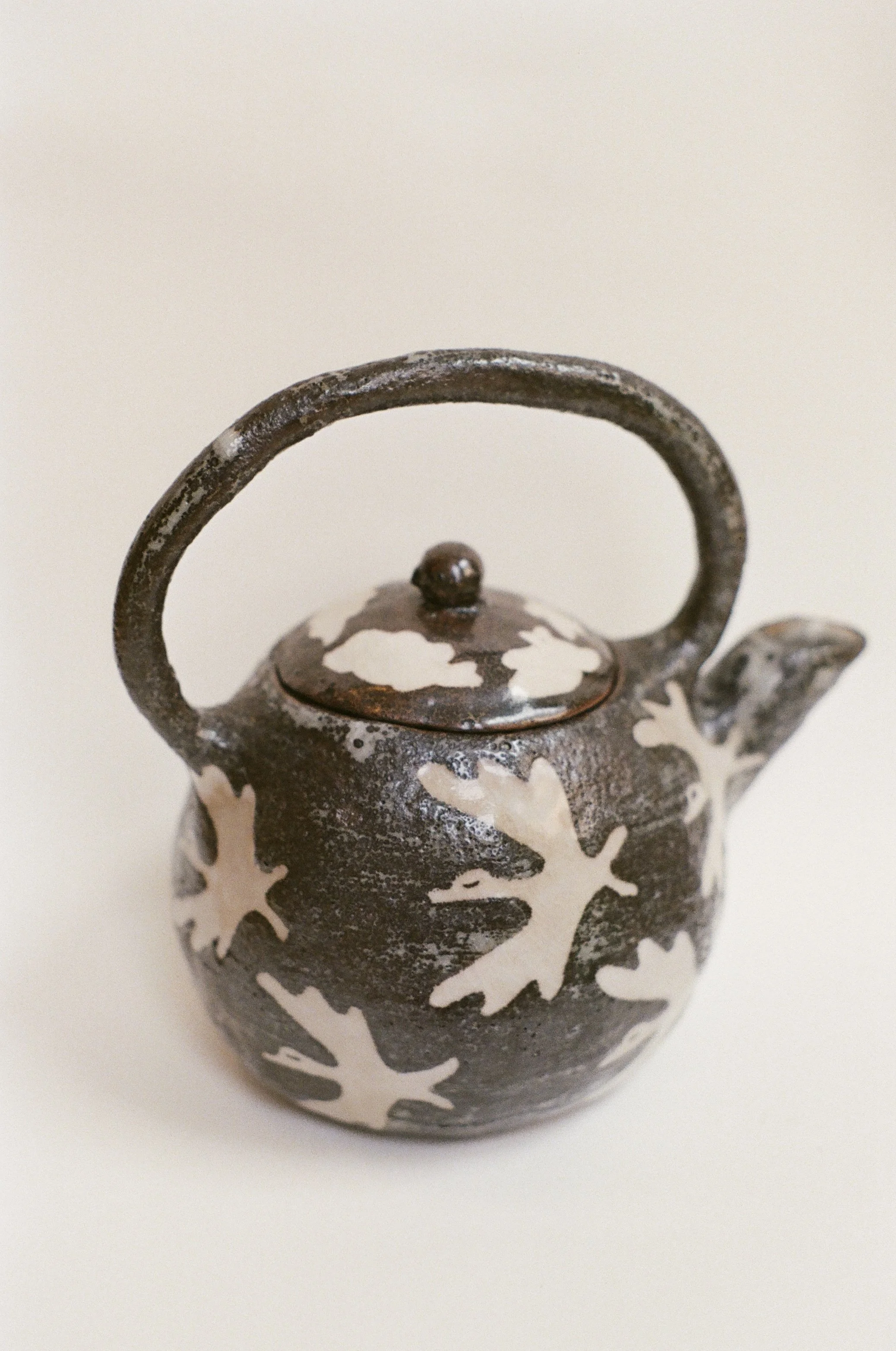 Close-up of a decorative teapot with a black and white floral design and a curved handle.