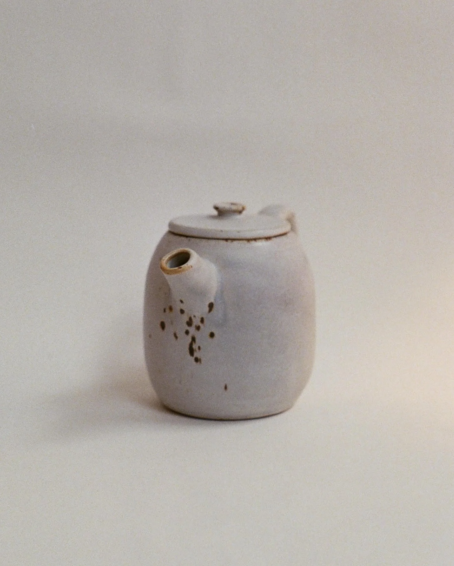 A white ceramic teapot with decorative holes and a small lid on top, placed against a neutral background.