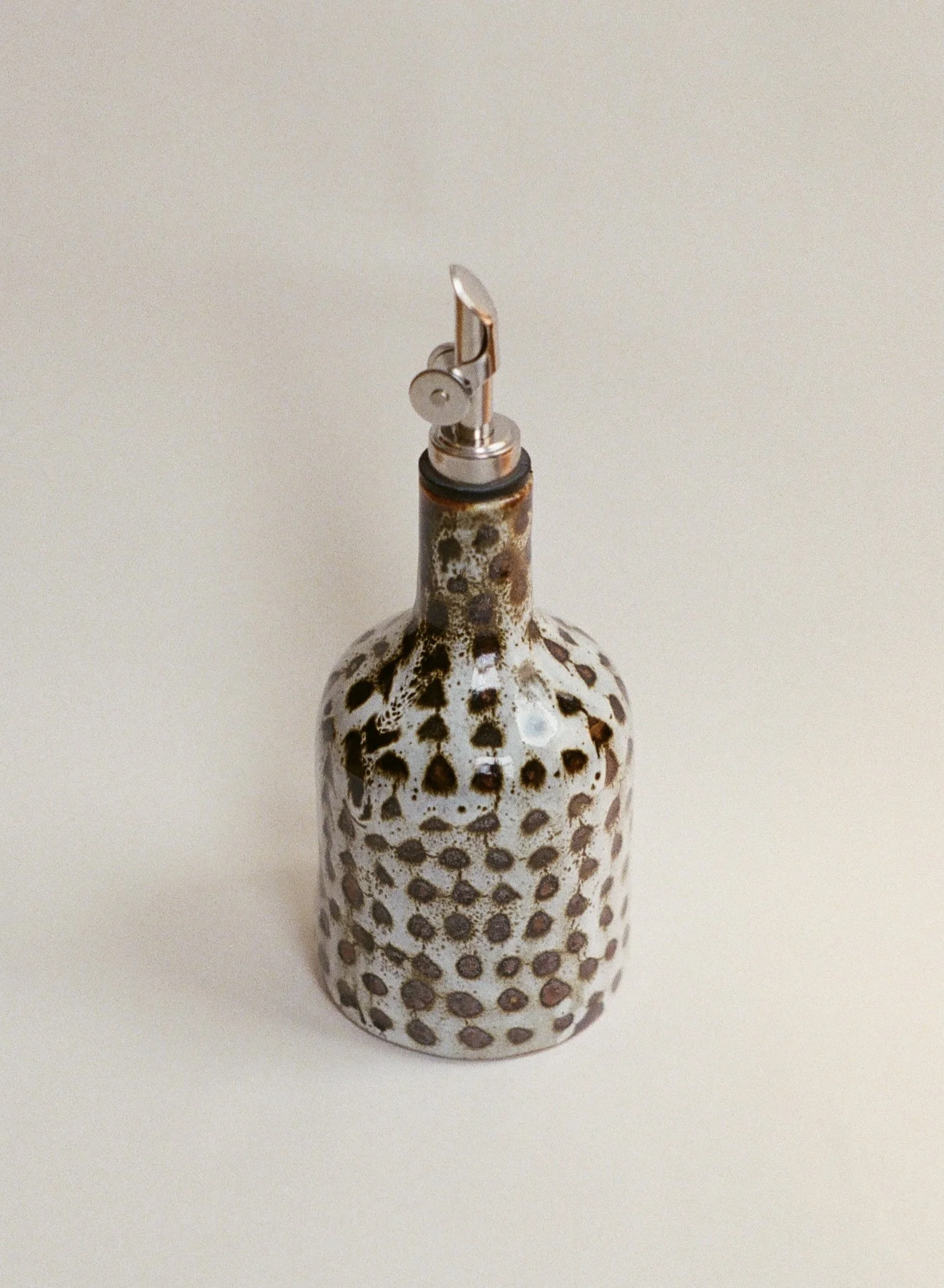 Ceramic vase with a rounded body and narrow neck, decorated with brown and cream spotted pattern, topped with a metallic clipper tool.