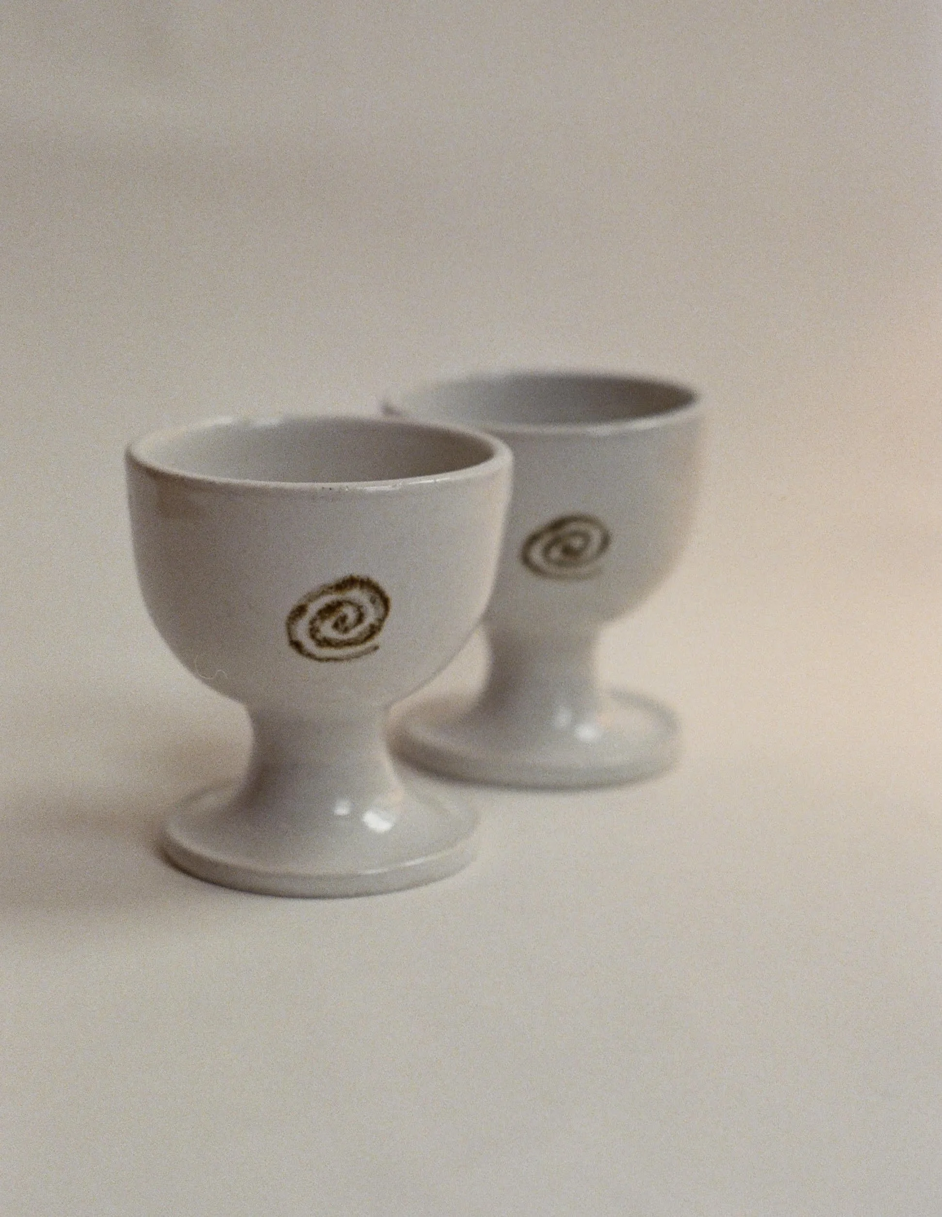 Two white ceramic goblets with spiral patterns, placed on a plain white surface with a neutral background.