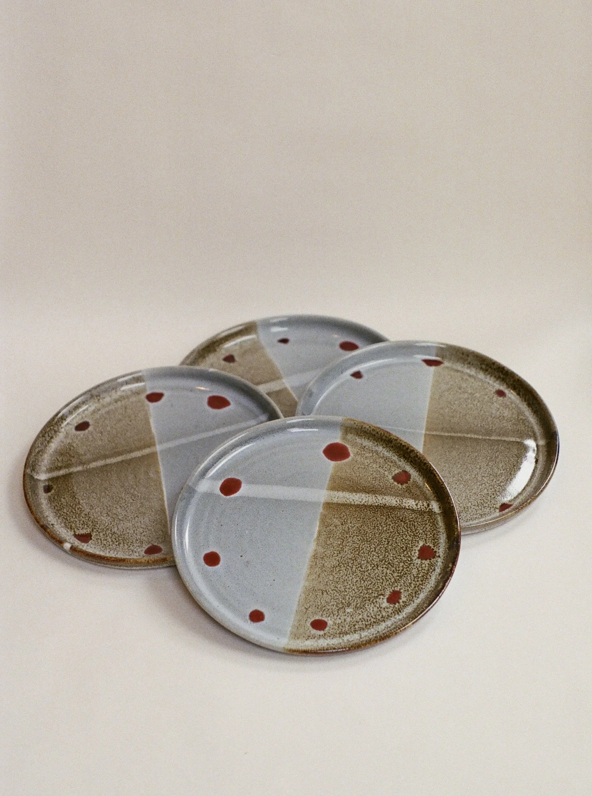 Six small oval ceramic bowls with a design of brown and white sections and red polka dots, arranged in a cluster on a white surface.