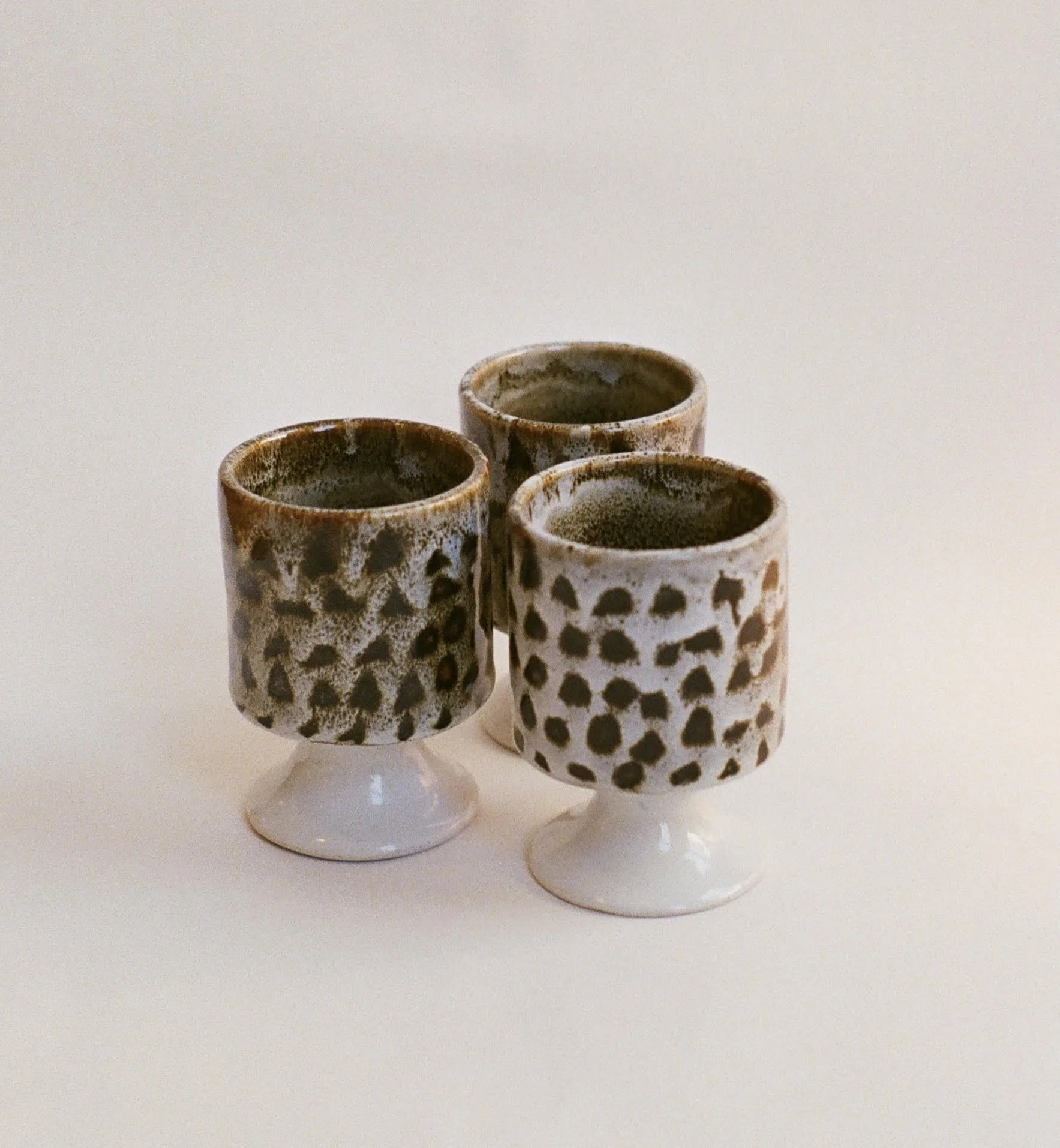 Four small ceramic cups with dark liquid, arranged on a white surface with a plain off-white background.