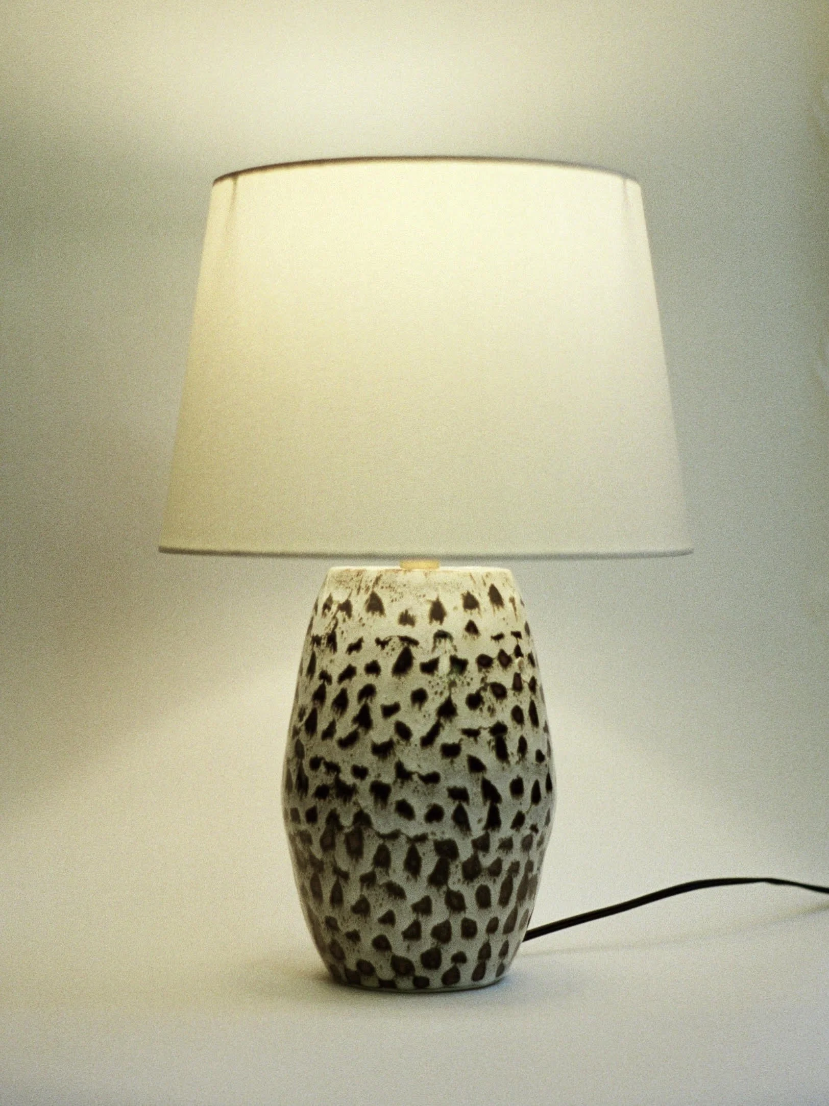 Decorative ceramic vase with black spots and a cutout pattern, placed on a plain surface.