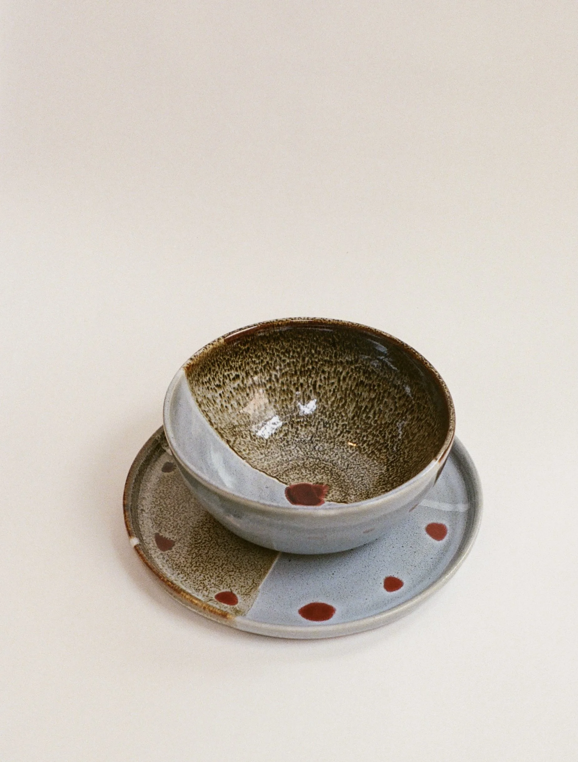 A white cup with a dark brown and gold speckled interior, sitting on a matching saucer with red dot accents, all on a white surface.