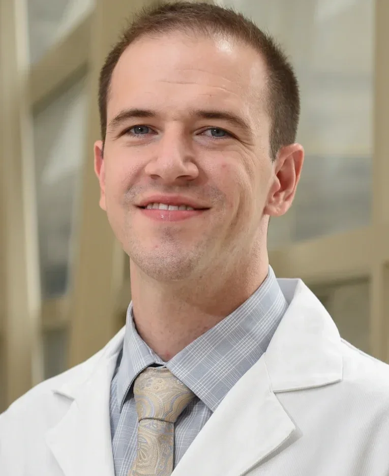 A male doctor in a white coat standing in a medical environment.