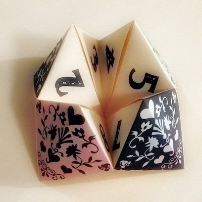 An early 2000s folded paper fortune teller called a cootie catcher feauring multiple sides with images and numbers to unfold that will reveal one's fortune.