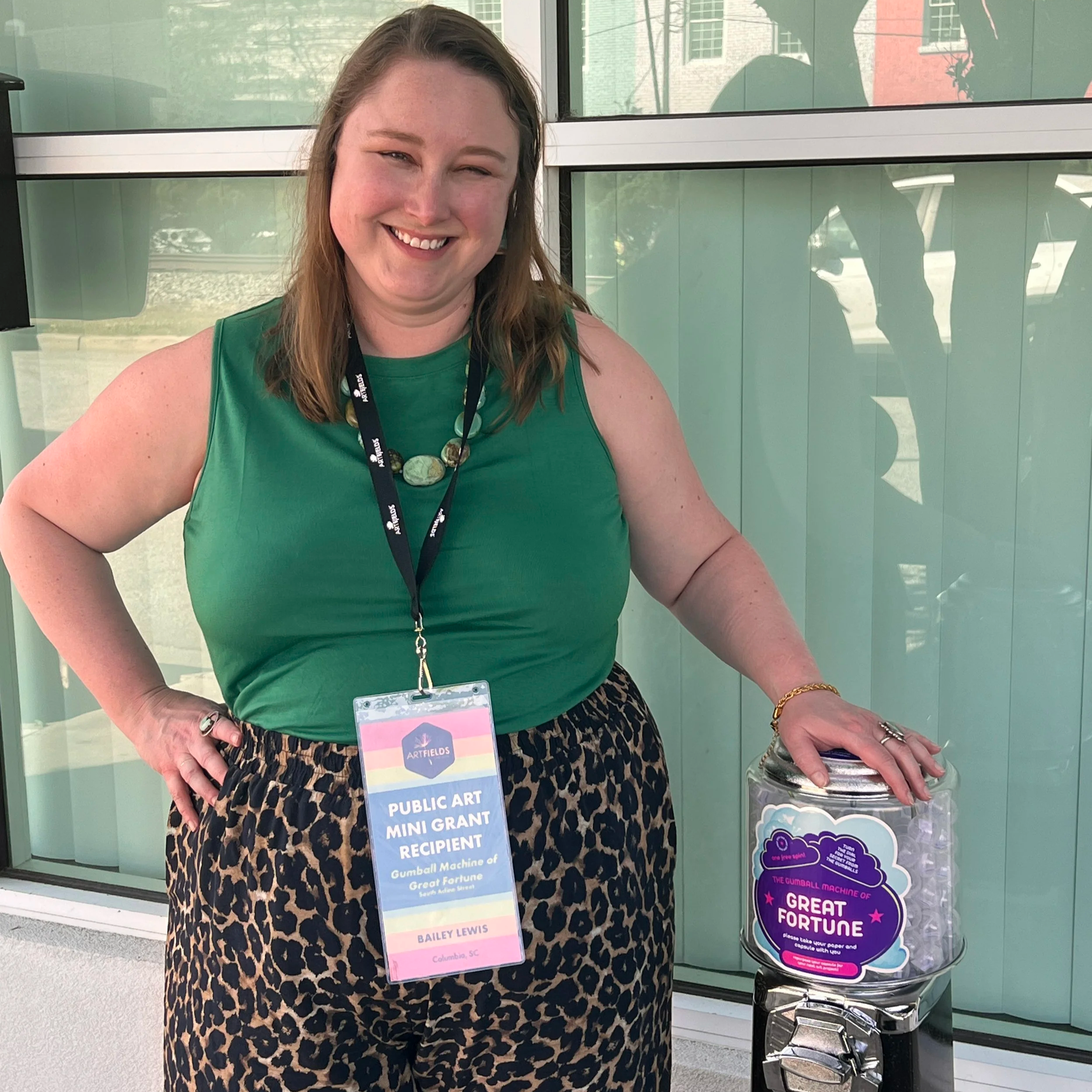 Bailey Lewis stands with her public installation, an interactive storytelling encounter called The Gumball Machine of Great Fortune at ArtFields 2026.