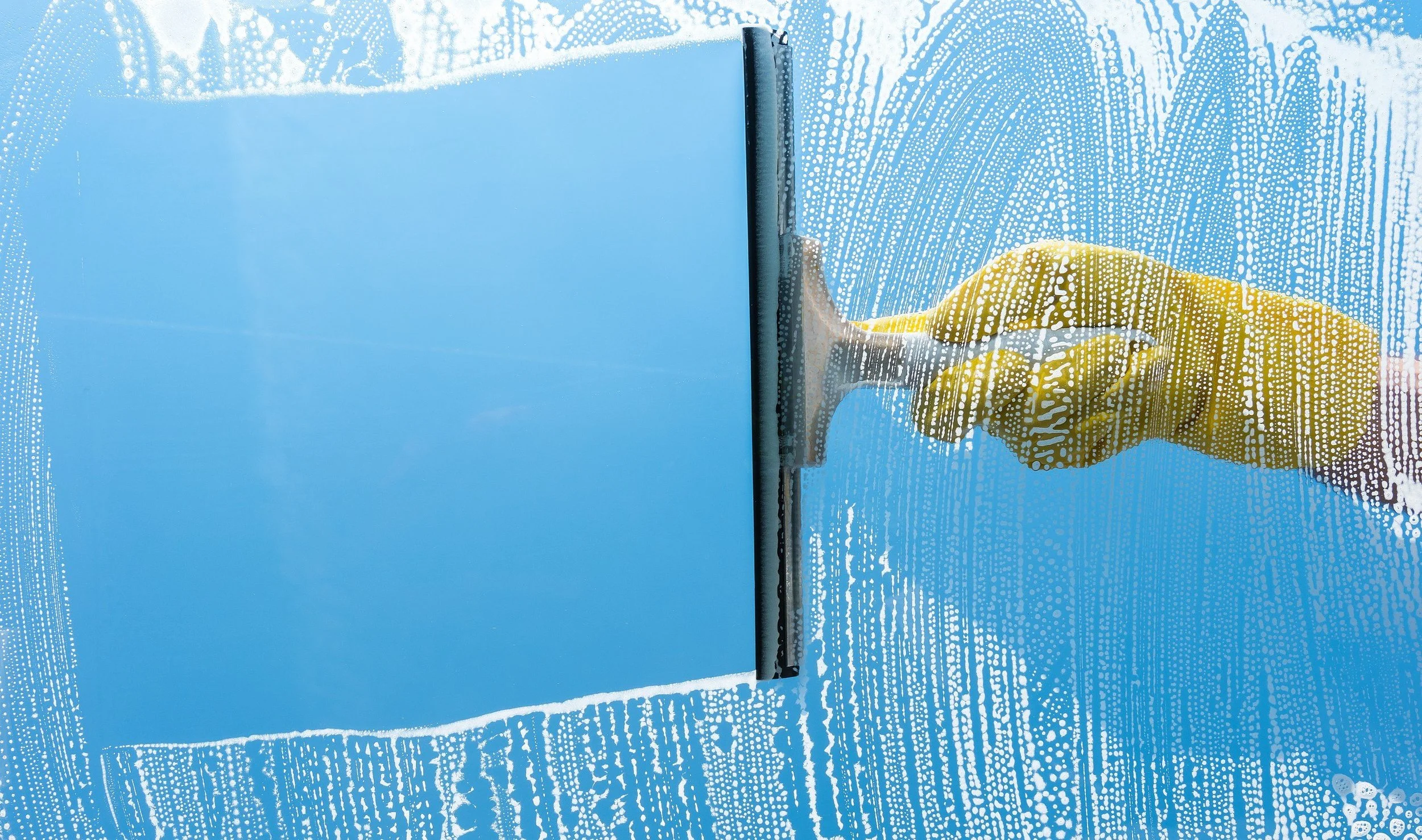 A person cleaning a glass window with a squeegee, seen through the wet glass with water droplets.