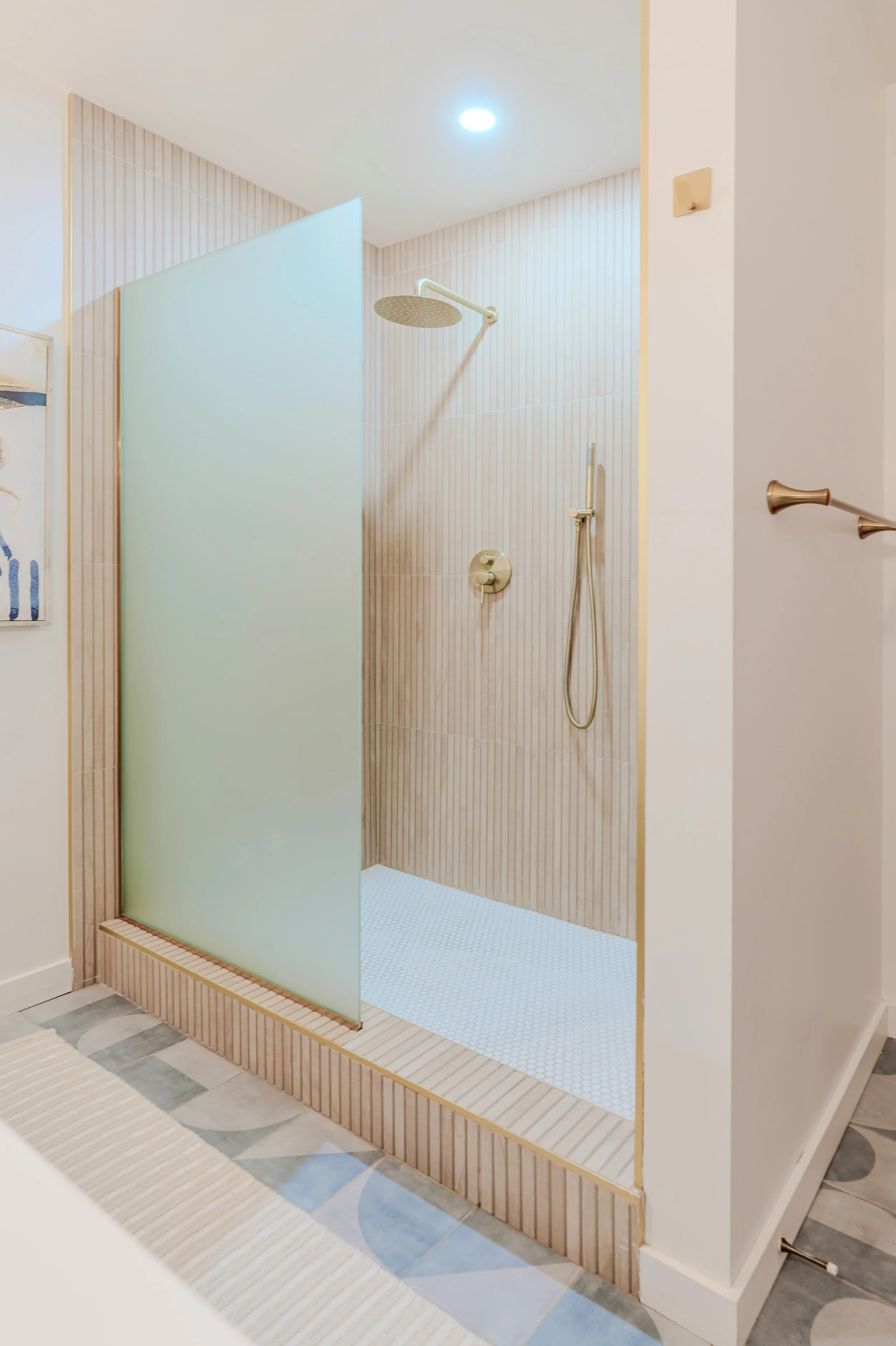 Shower with beige striped walls, a large rain showerhead, a handheld shower, and a frosted glass partition.