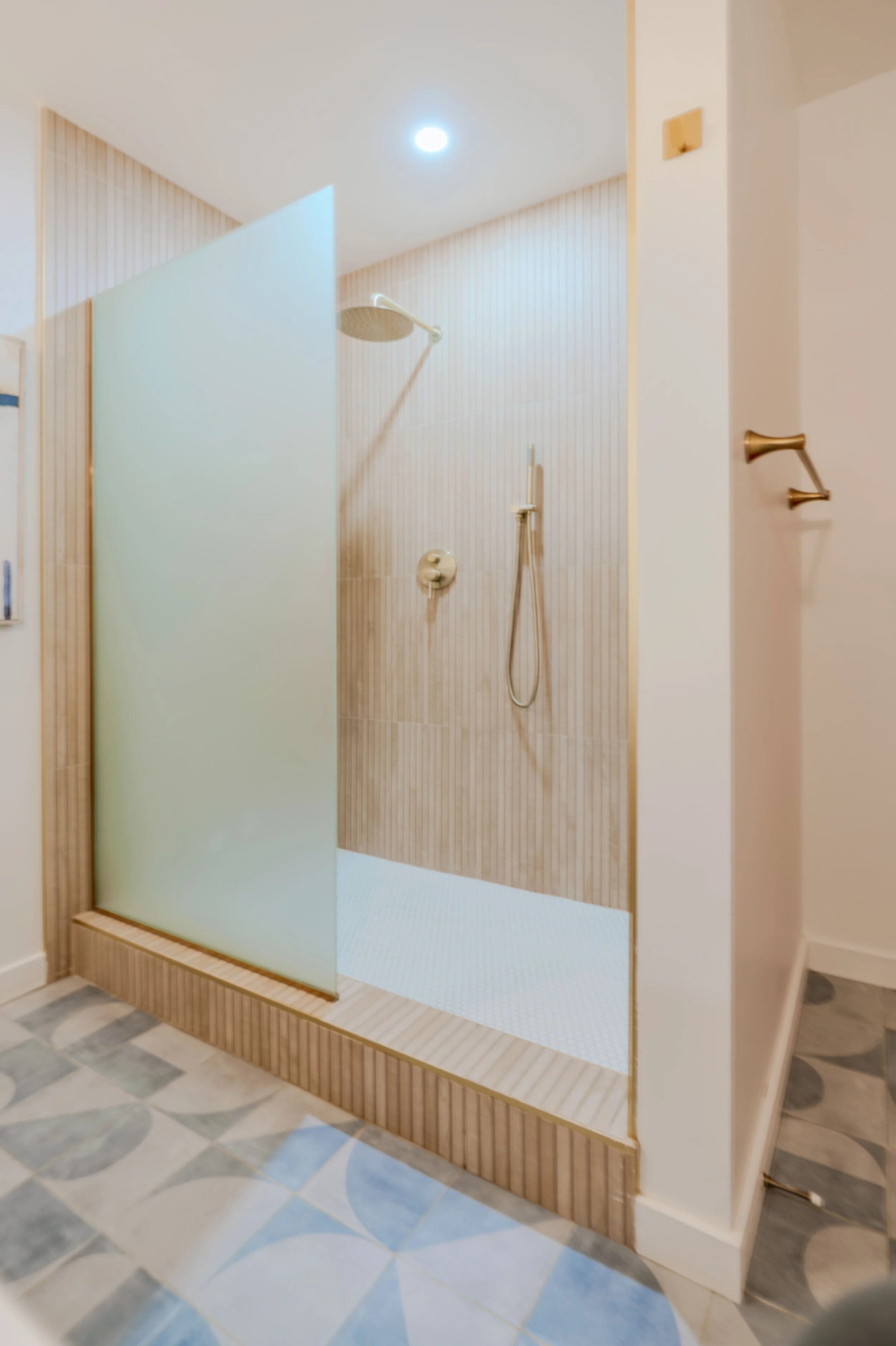 Modern bathroom shower with a frosted glass door and wooden frame, wall-mounted showerhead, and tiled walls, located on a marble floor with geometric pattern.