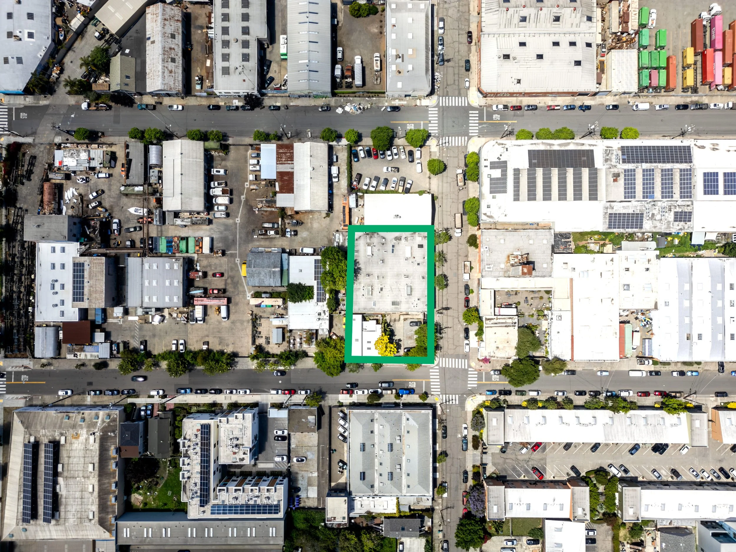 An aerial view of a city block with buildings, parking lots, trees, and streets with cars.
