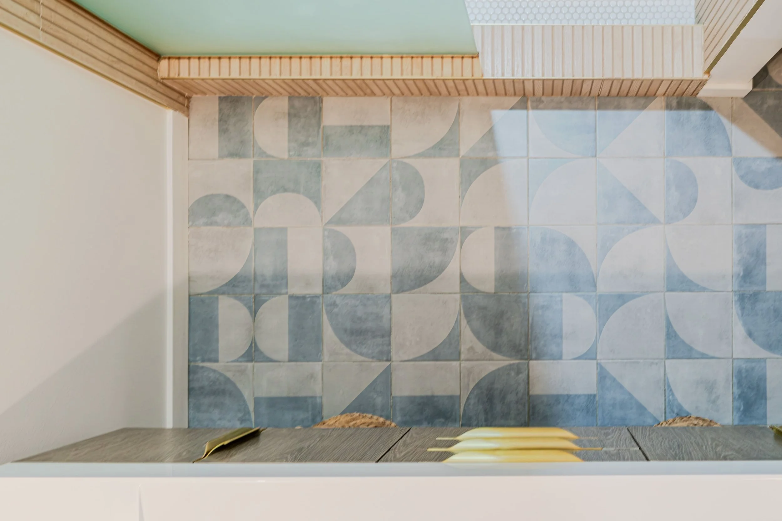 Top view of a bathroom with patterned floor tiles, a wooden bench, and slippers on the mat.