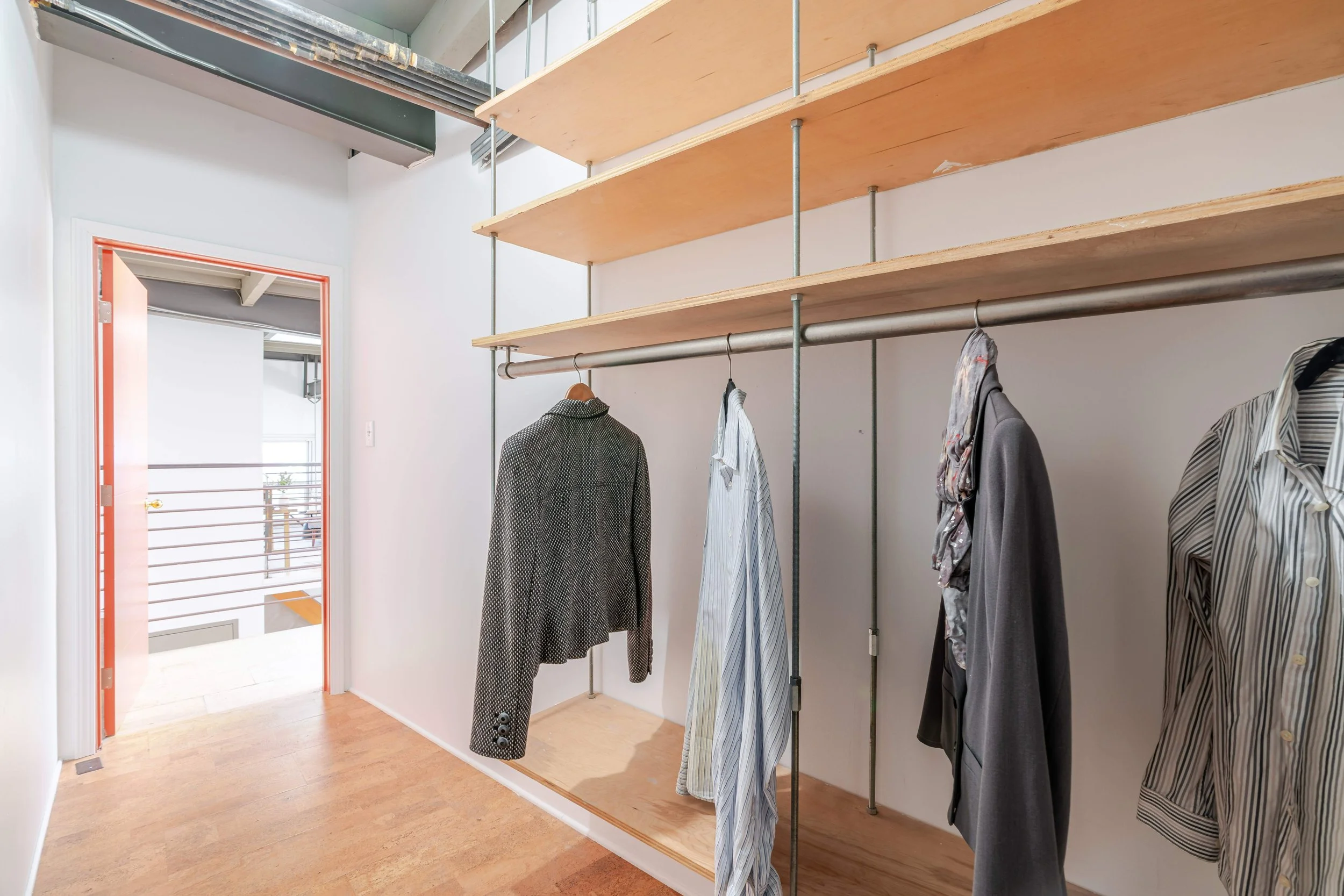 Closet with hanging clothes, wooden shelves, and part of a door leading to an outdoor balcony.
