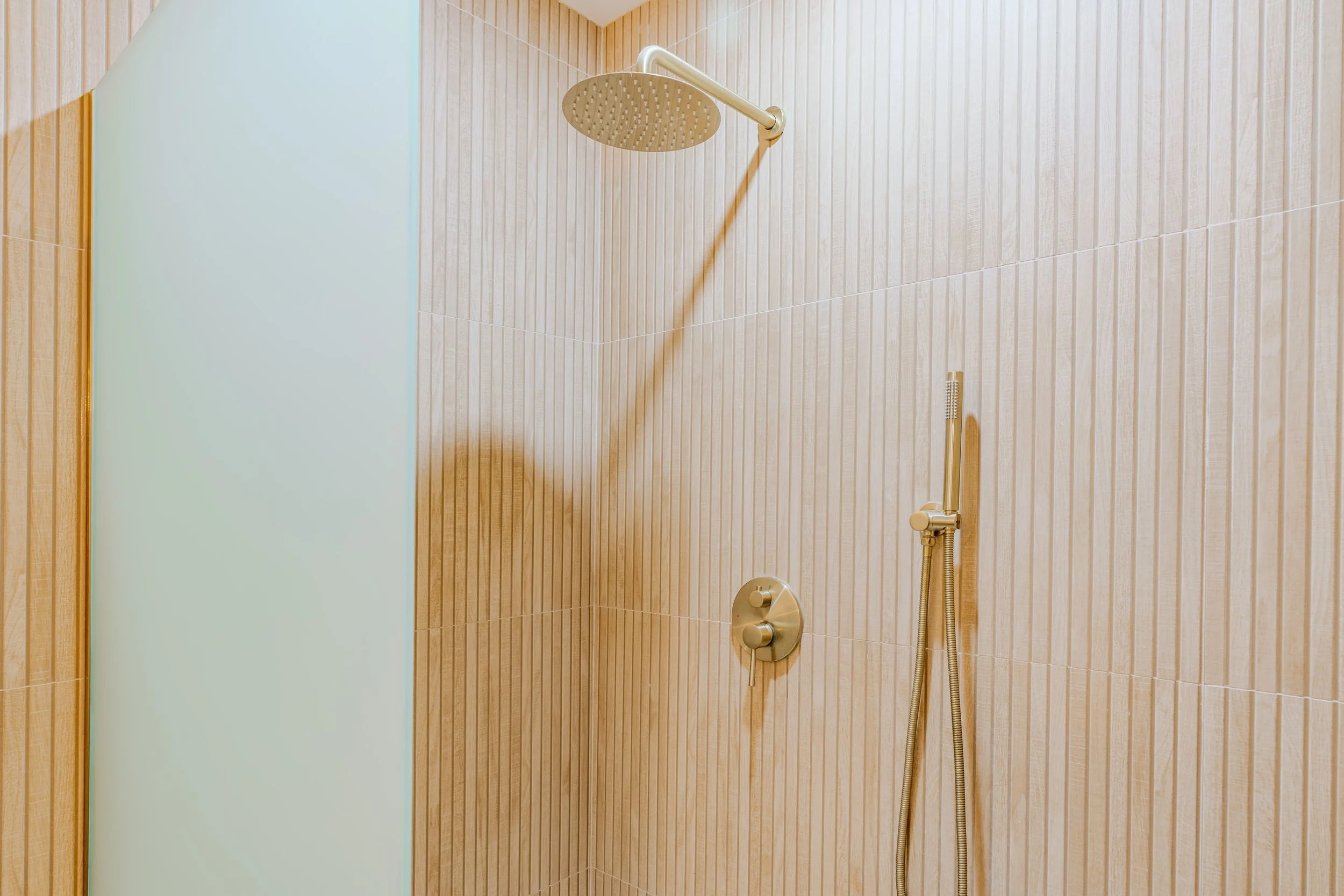 Shower with a rain shower head mounted on a wooden wall with a handheld shower head attached.