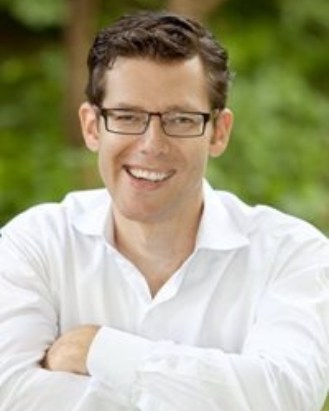 Lächelnder Mann mit Brille in weißem Hemd vor grünem Hintergrund.