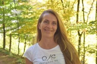 Lächelnde Frau mit langem Haar in einem Park im Herbst, Sonnenlicht durch die Bäume