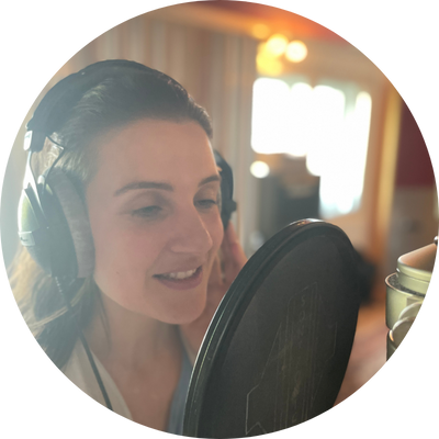 Eine Frau im Aufnahmestudio mit Kopfhörern vor einem Mikrofon, die singt oder spricht.