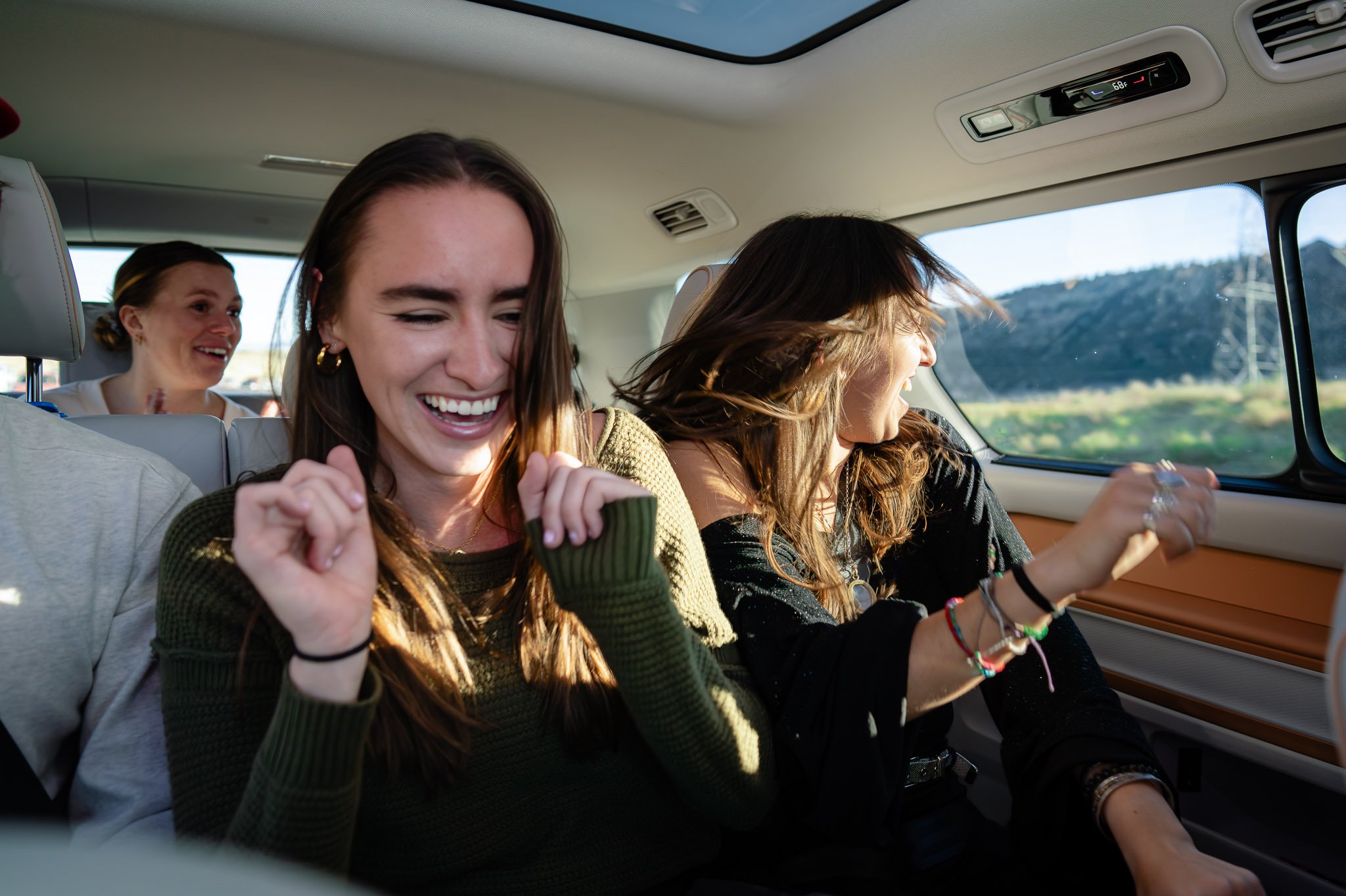 Four women are sitting and smiling inside the VIP Red Rocks bus, with a view of mountains and the sky outside the window and panaromic sunroof.