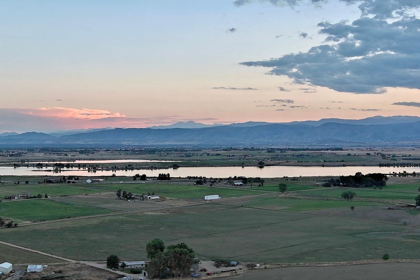 A peaceful landscape with fields, a river, and mountains in the distance during sunset.