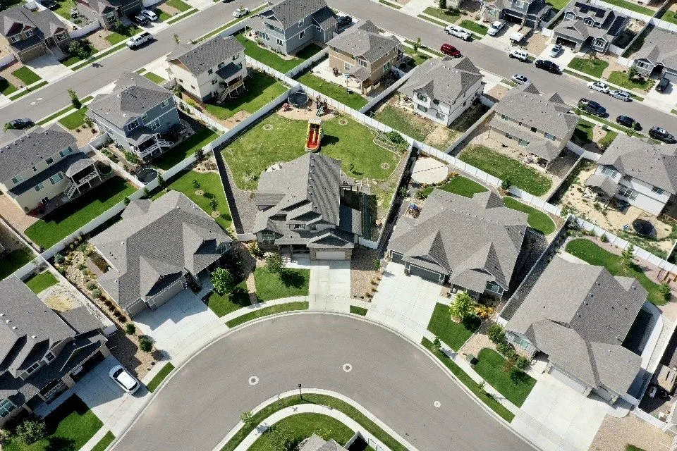 Aerial view of a suburban neighborhood with single-family homes, streets, driveways, and a backyard with a play structure.