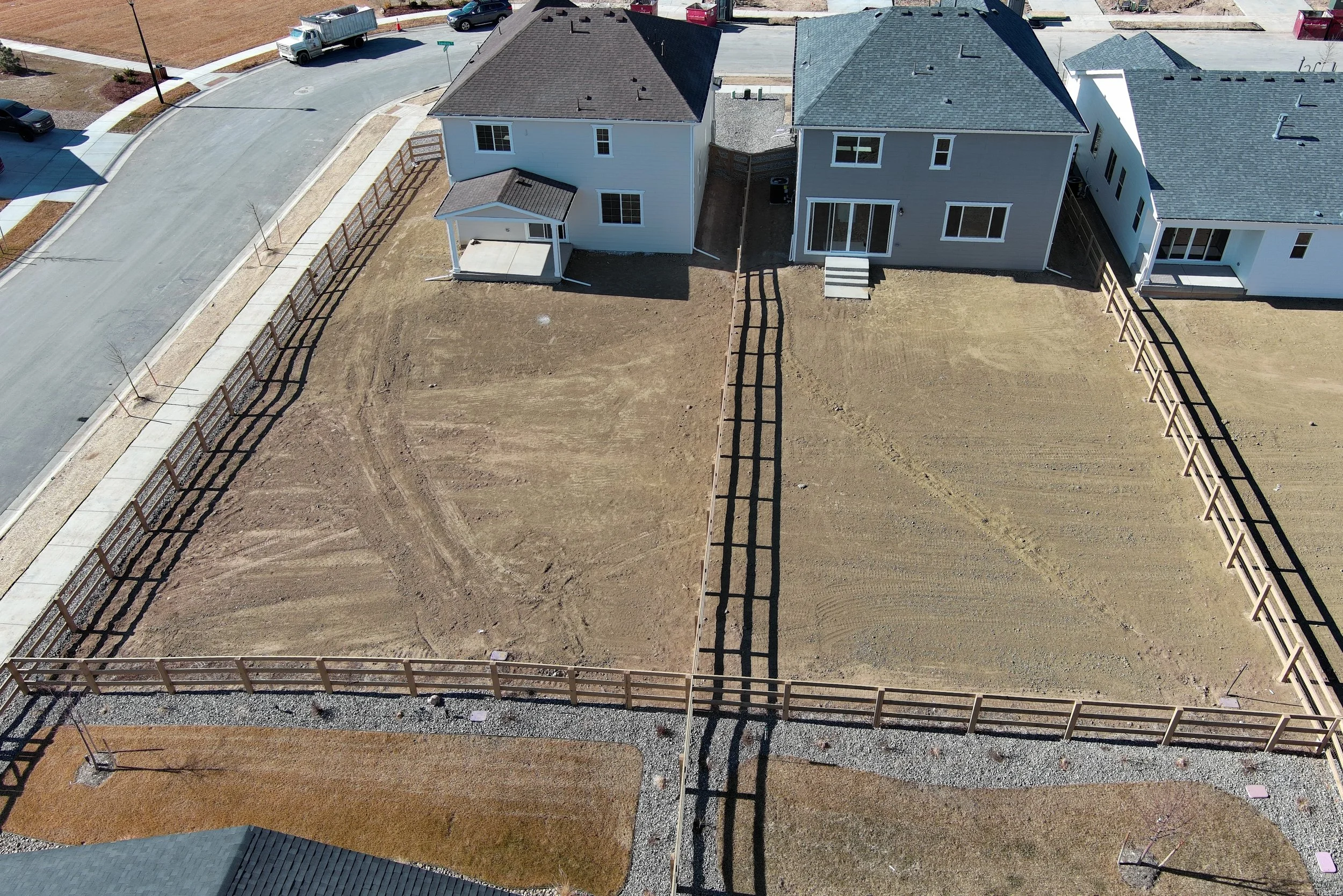 Aerial view of a residential area showing a row of houses with driveways, fences, and front yards under construction or landscaping.