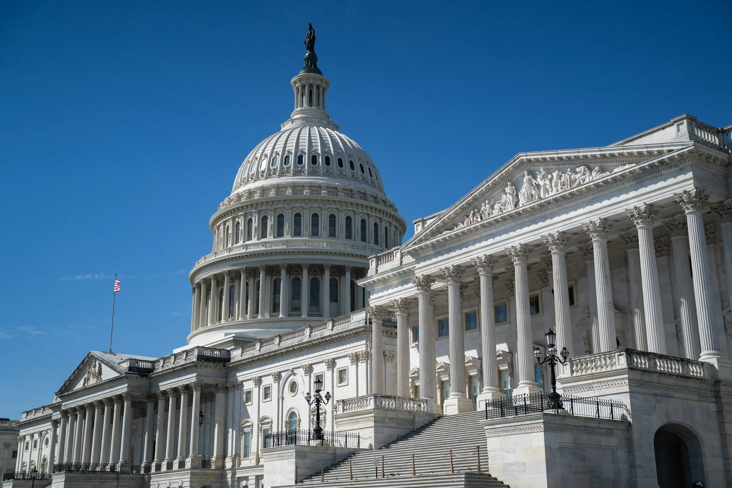 The United States Capitol building with a prominent dome, columns, and architectural sculptures, under a clear blue sky.