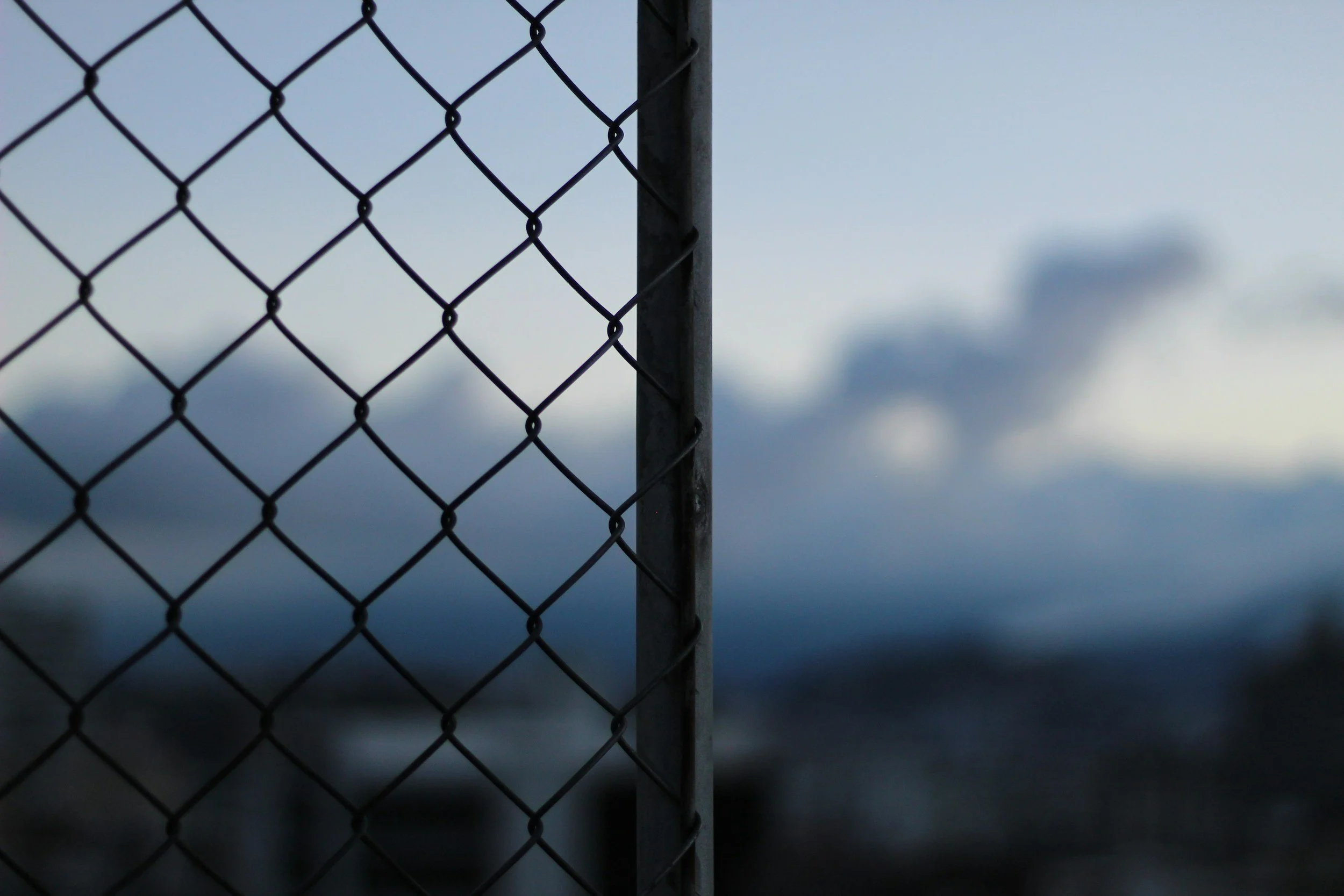 A black chain-link fence with a metal support post against a cloudy sky.